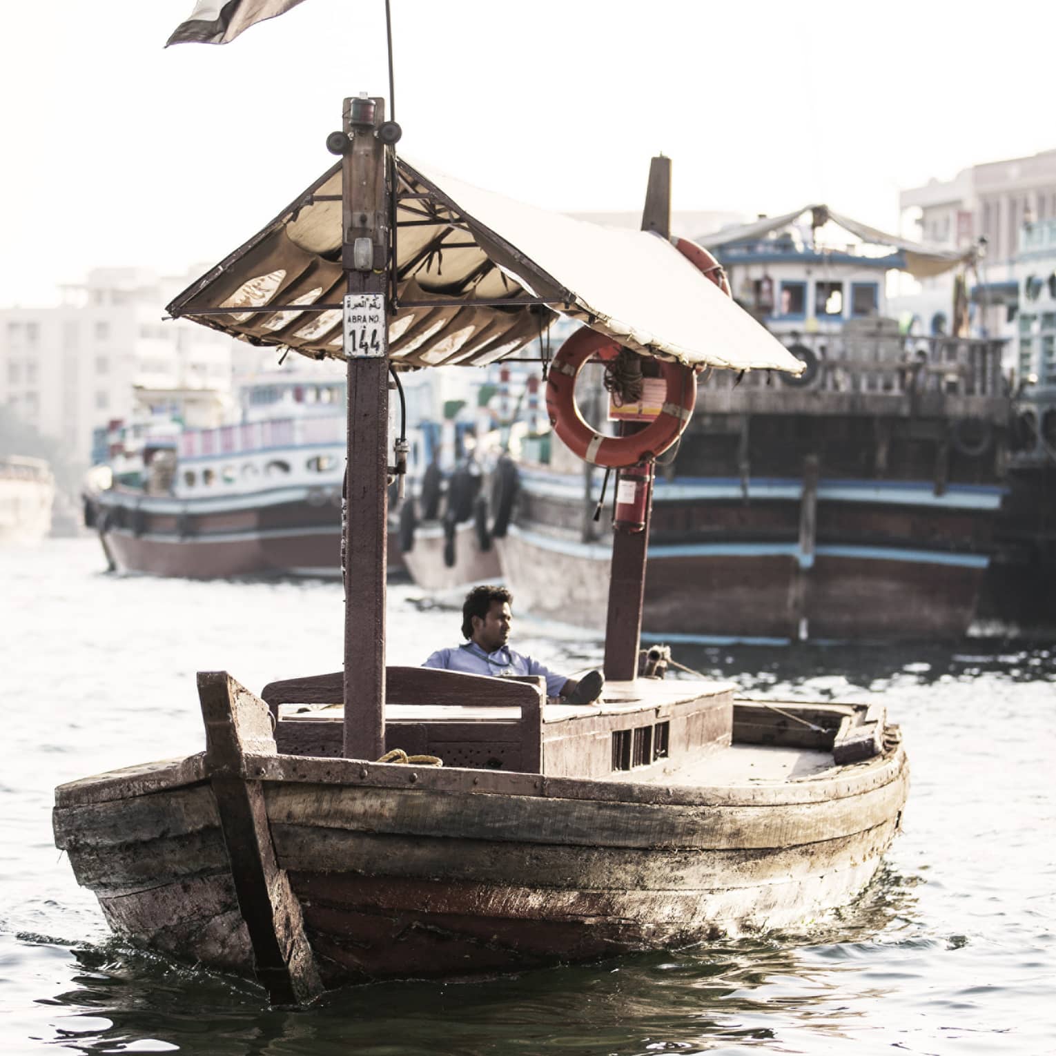 A small wooden boat flying the UAE flag as it sails down a small waterway. 