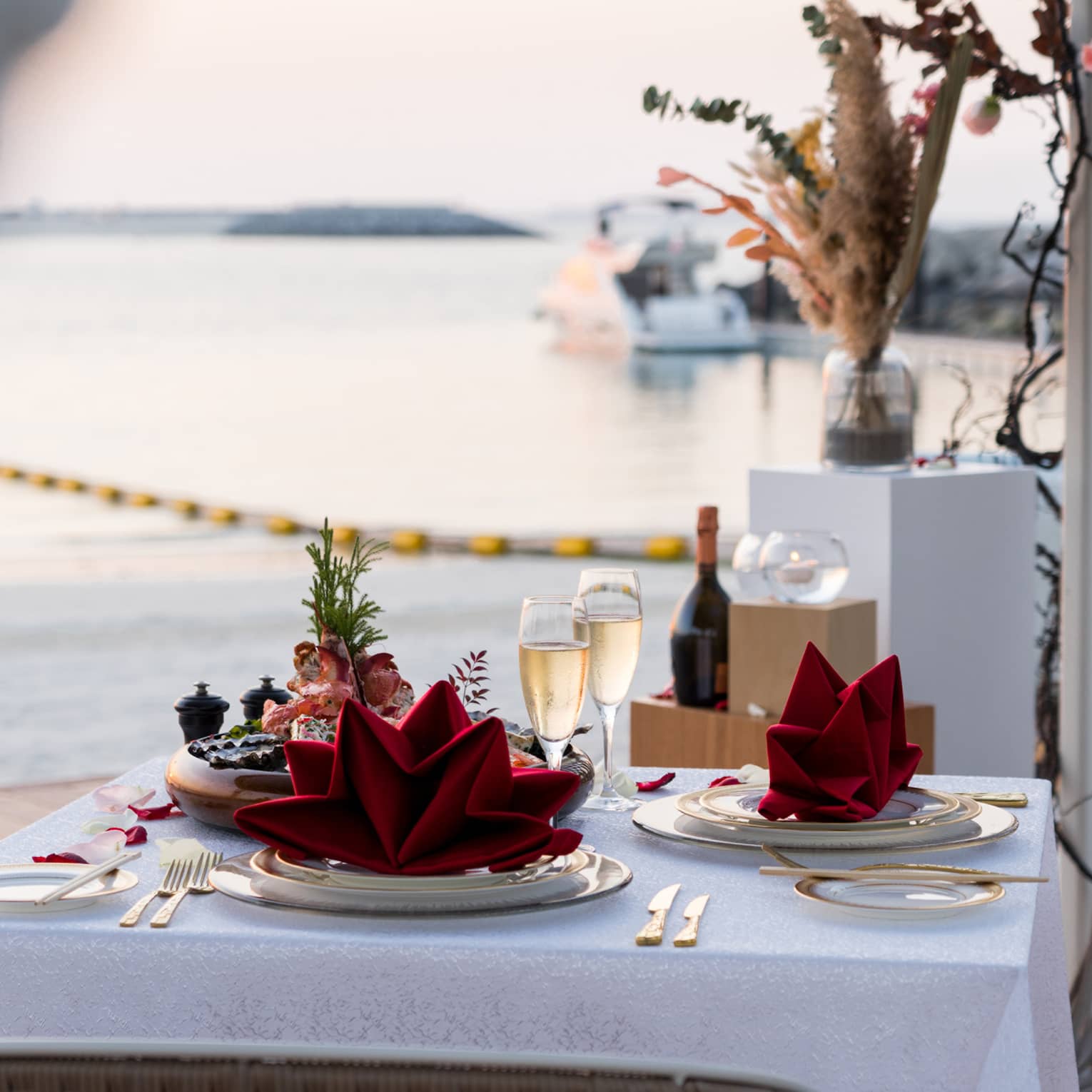 A table set for two with two glasses of champagne on a pier overlooking a calm sea.