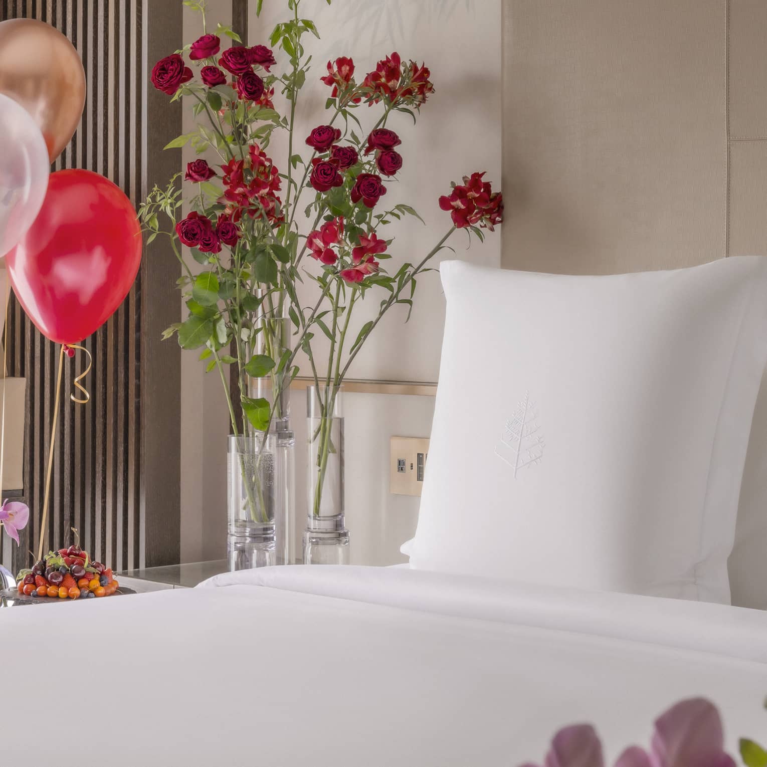 King bed with white linens surrounded by colourful balloons and ice bucket of champagne nearby