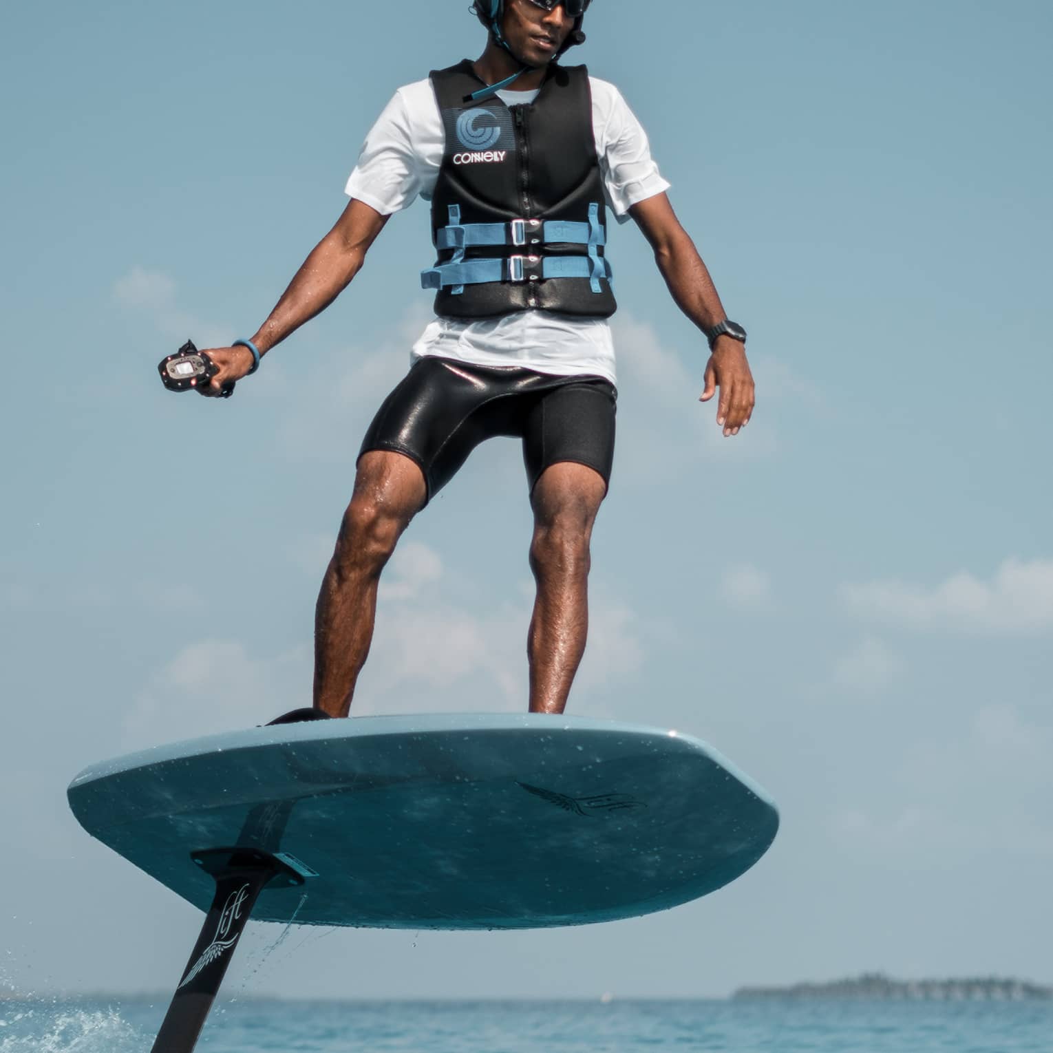 In a helmet and life jacket, an adventurer stands on an eFoil using a handheld control to propel the board out of the water.