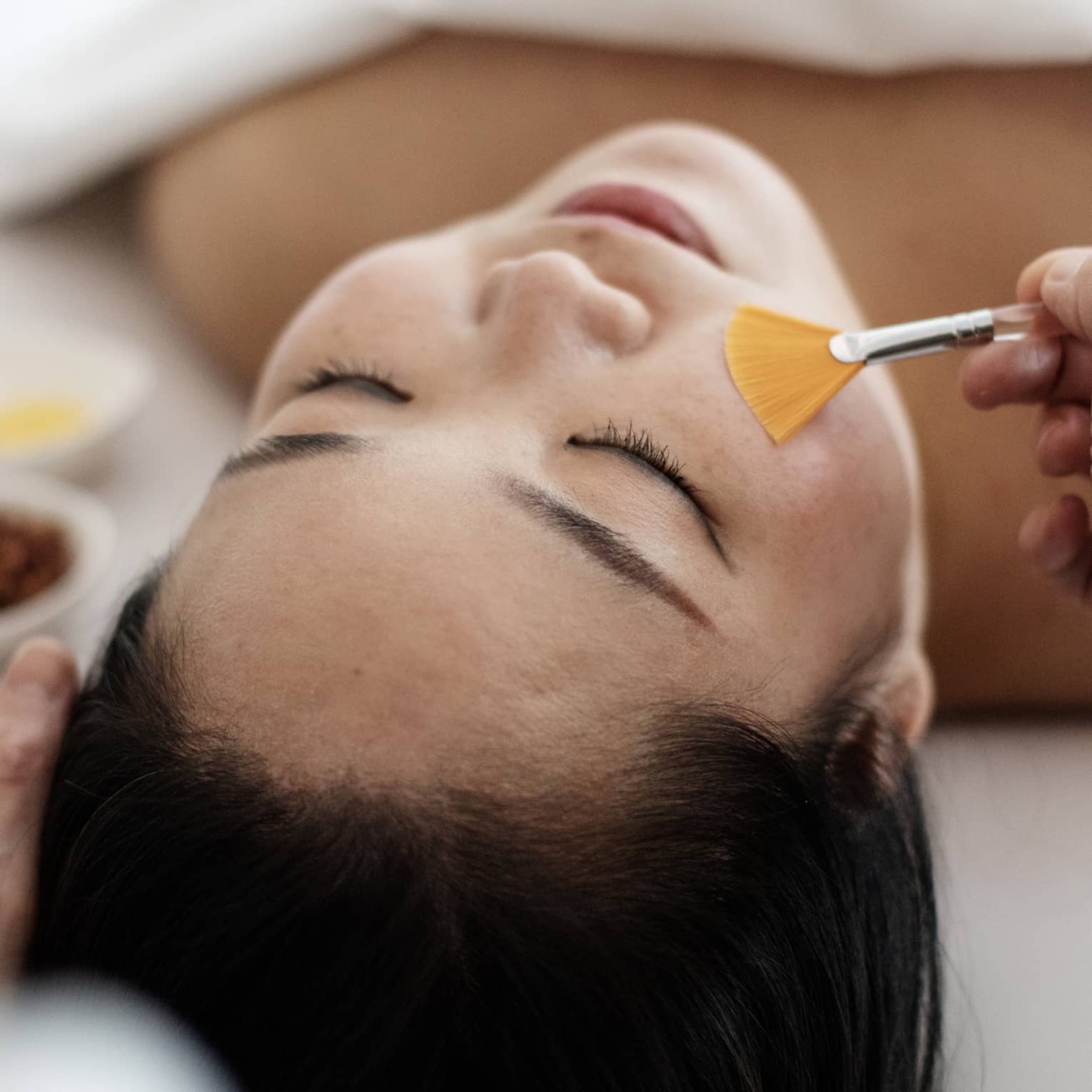 A woman receiving a spa treatment utilizing a brush on her face.