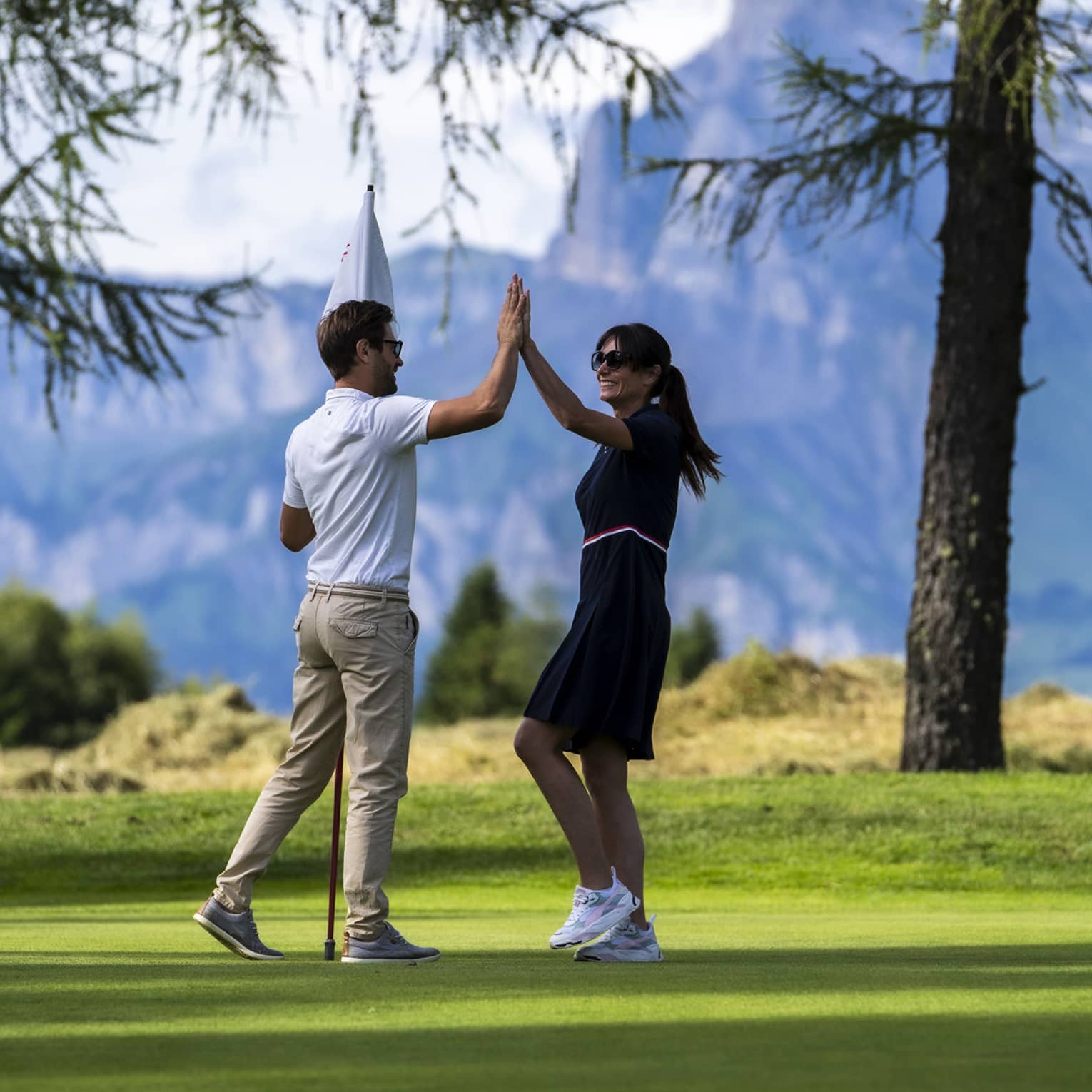 Two people high-fiving on a golf course with mountains in the distance