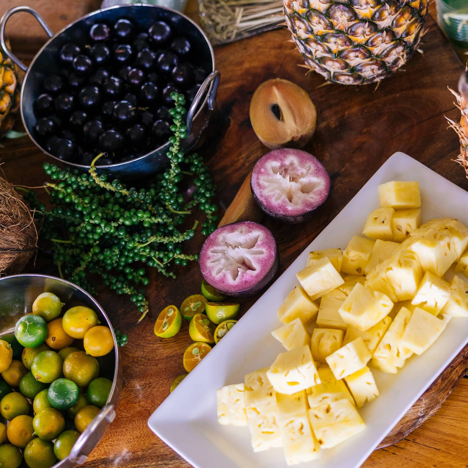 Table set with plate of cubed pineapple, bowl of berries, a halved coconut and other fruits