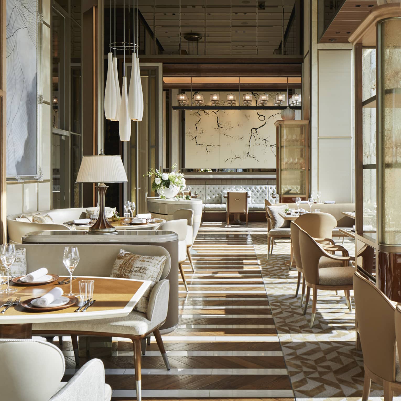 Est dining room with cream plush chairs, tables set with glassware, natural light, hardwood floors 