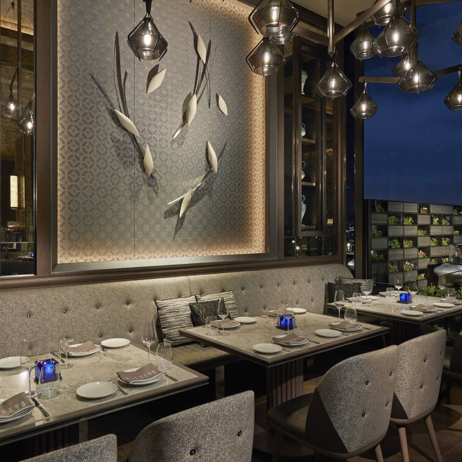 Tables set for two overlook nighttime skyline, floor-to-ceiling windows, intimate lighting, grey colour scheme 
