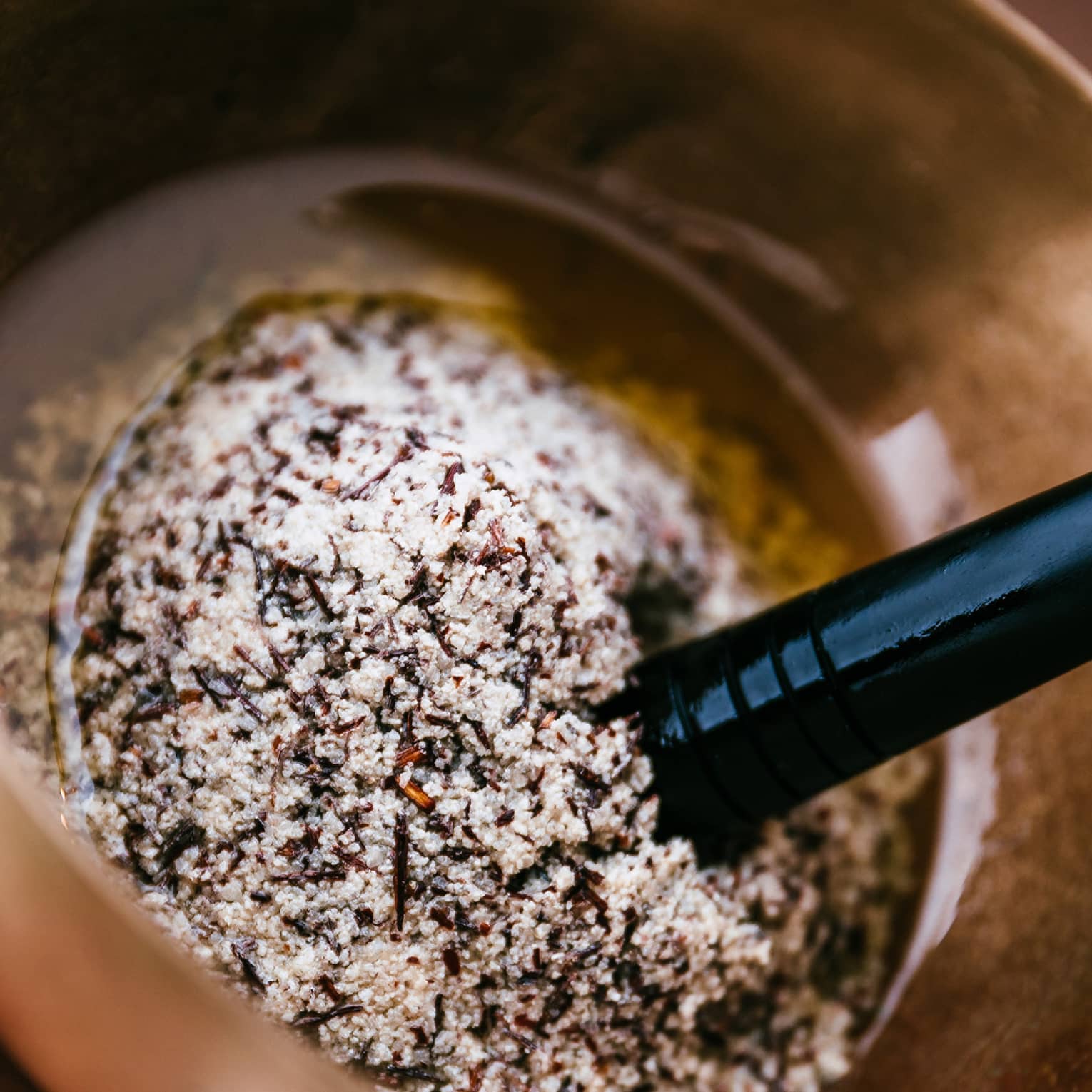 A person uses a golden mortar and pestle to grind several salts and spices into oil.
