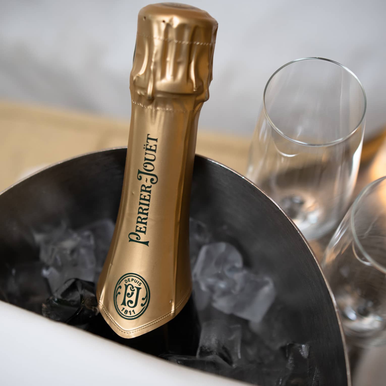 A bottle of Champagne in a bucket of ice with two glasses next to it.