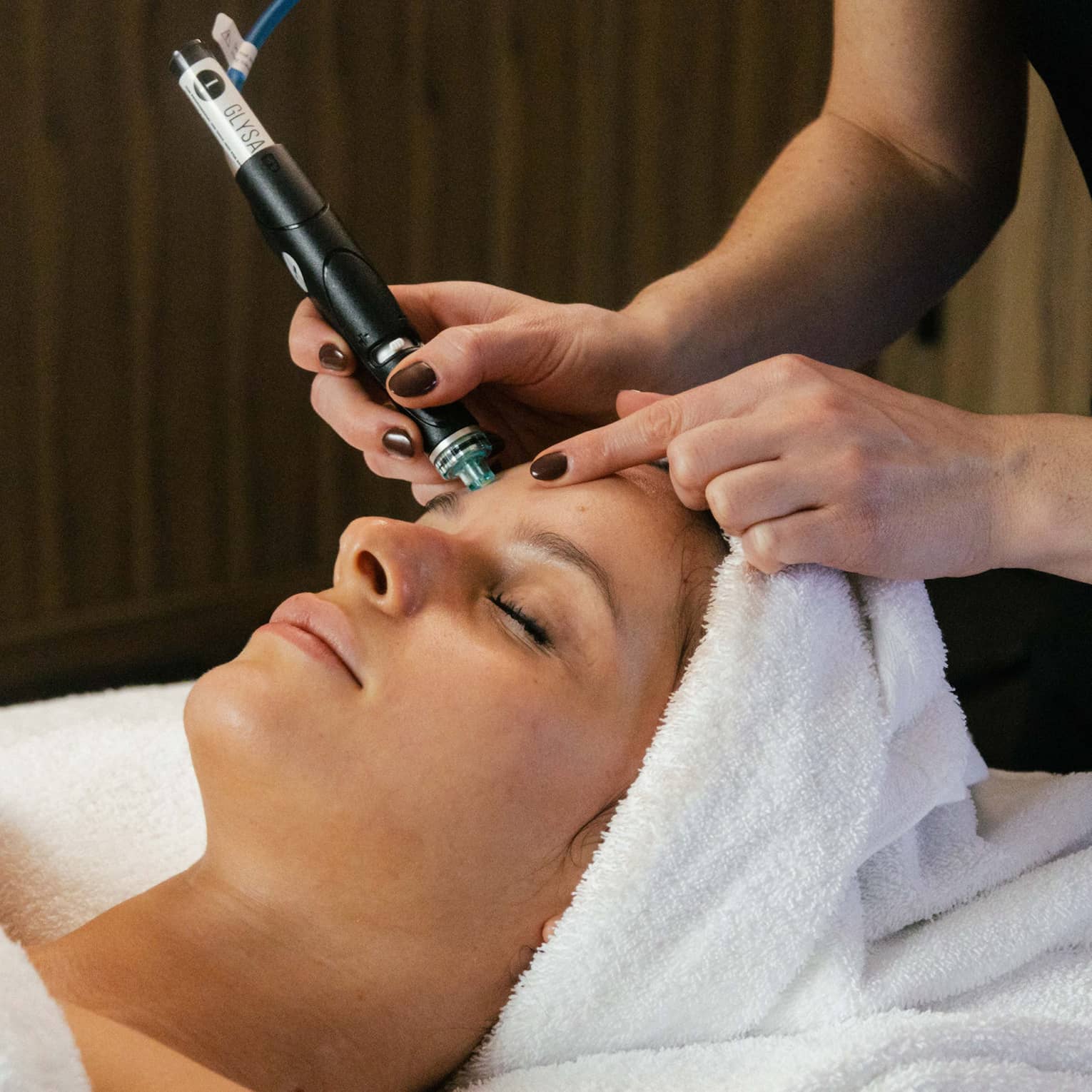 A guest laying on a spa table with a towel wrapped around their hair and getting a facial
