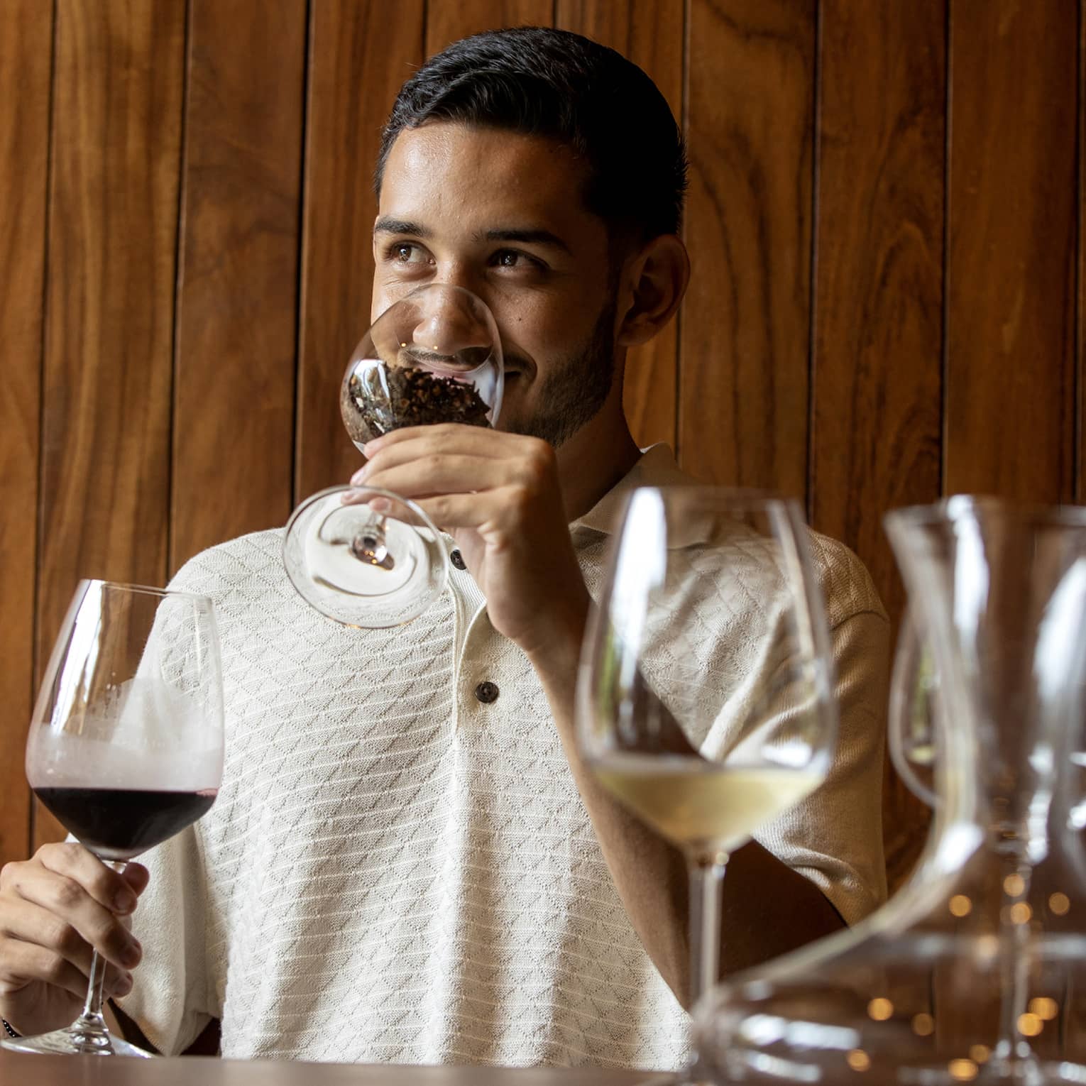 At a wine tasting, a guest smells coffee beans in a glass before tasting the glass of dark red wine held in his other hand. 