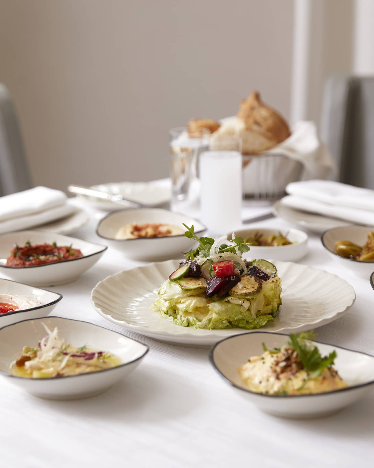 Small white dishes with lunch items, meats, breads, sauces on dining table