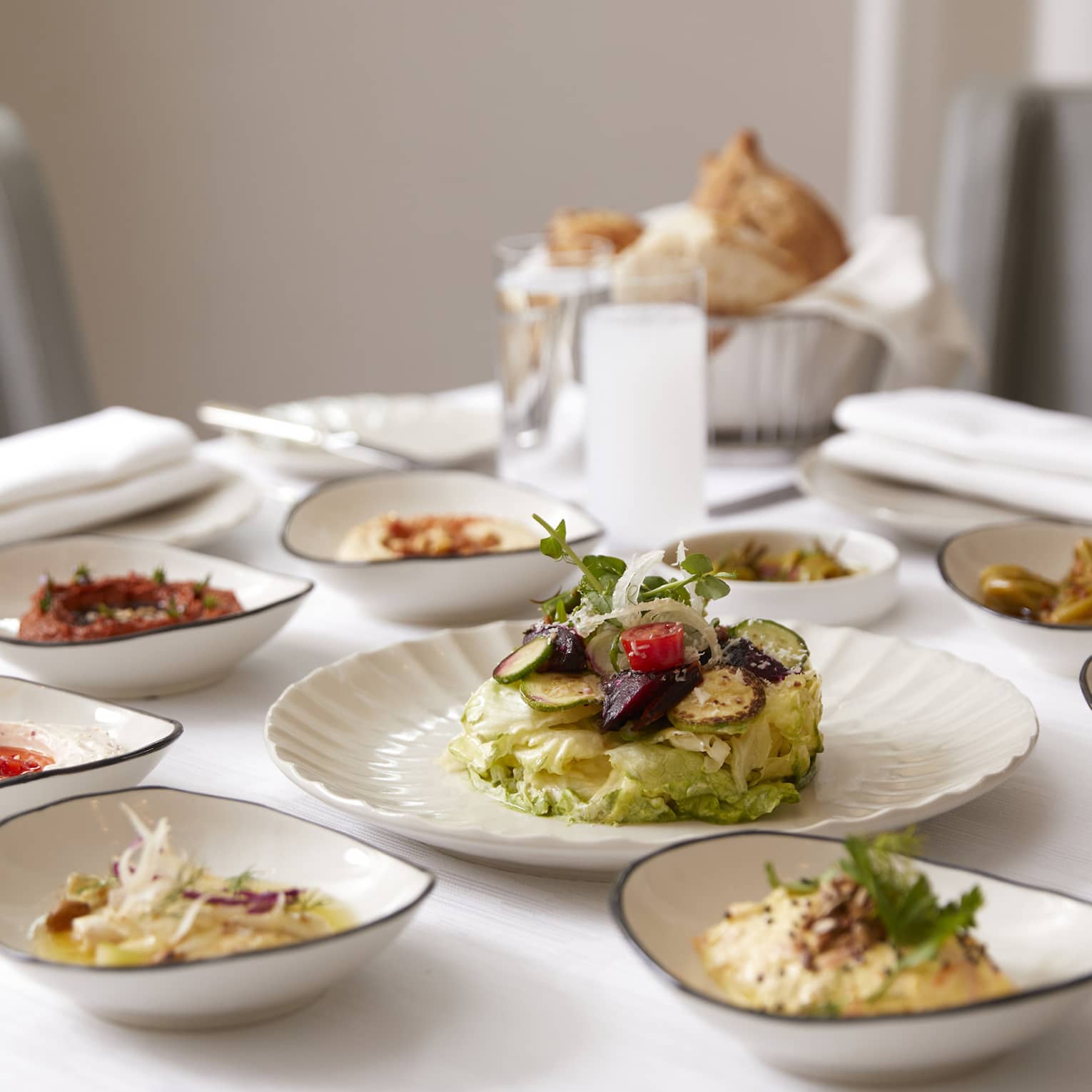 Small white dishes with lunch items, meats, breads, sauces on dining table