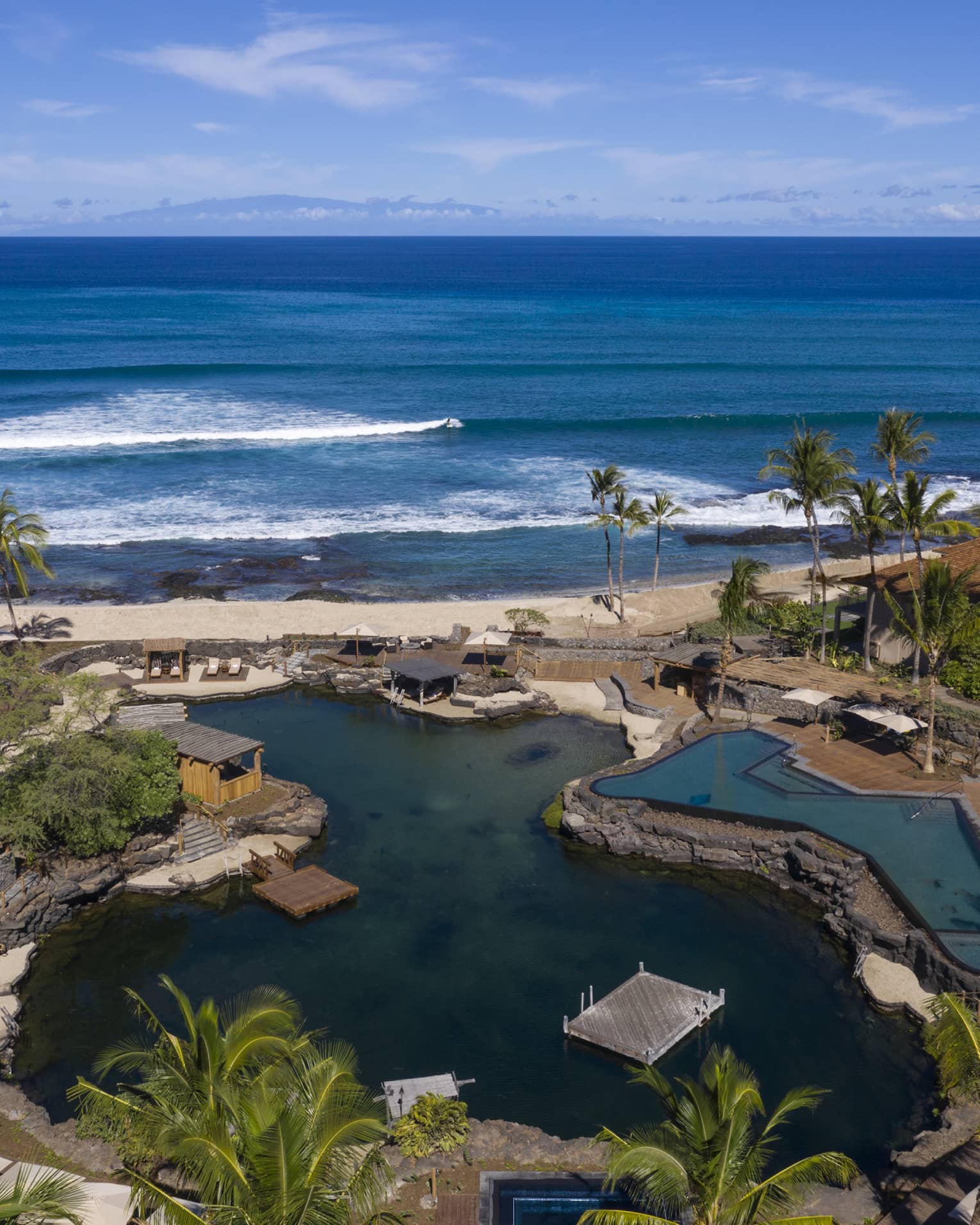 Aerial view of resort pool that mimics a curved pond, palm trees, beach and ocean