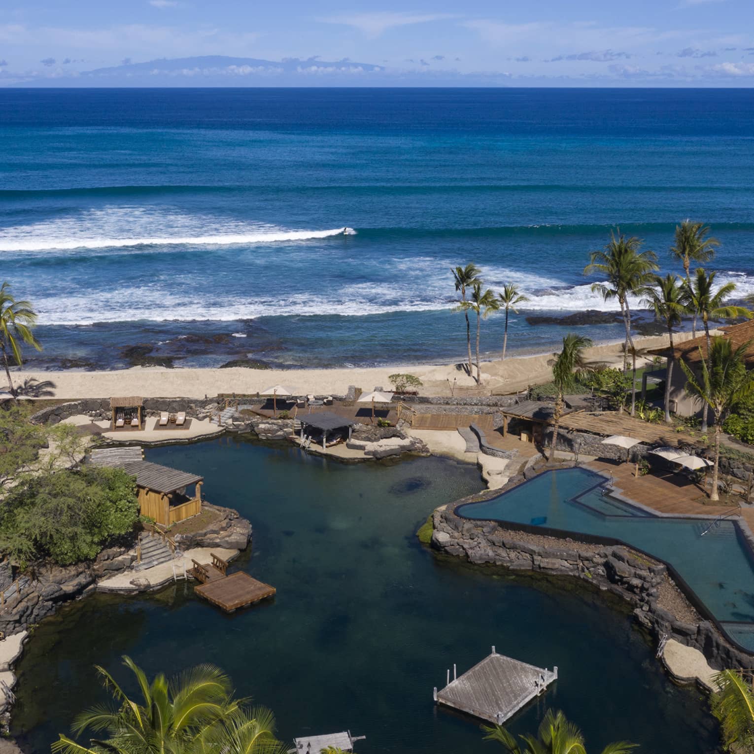 Aerial view of resort pool that mimics a curved pond, palm trees, beach and ocean