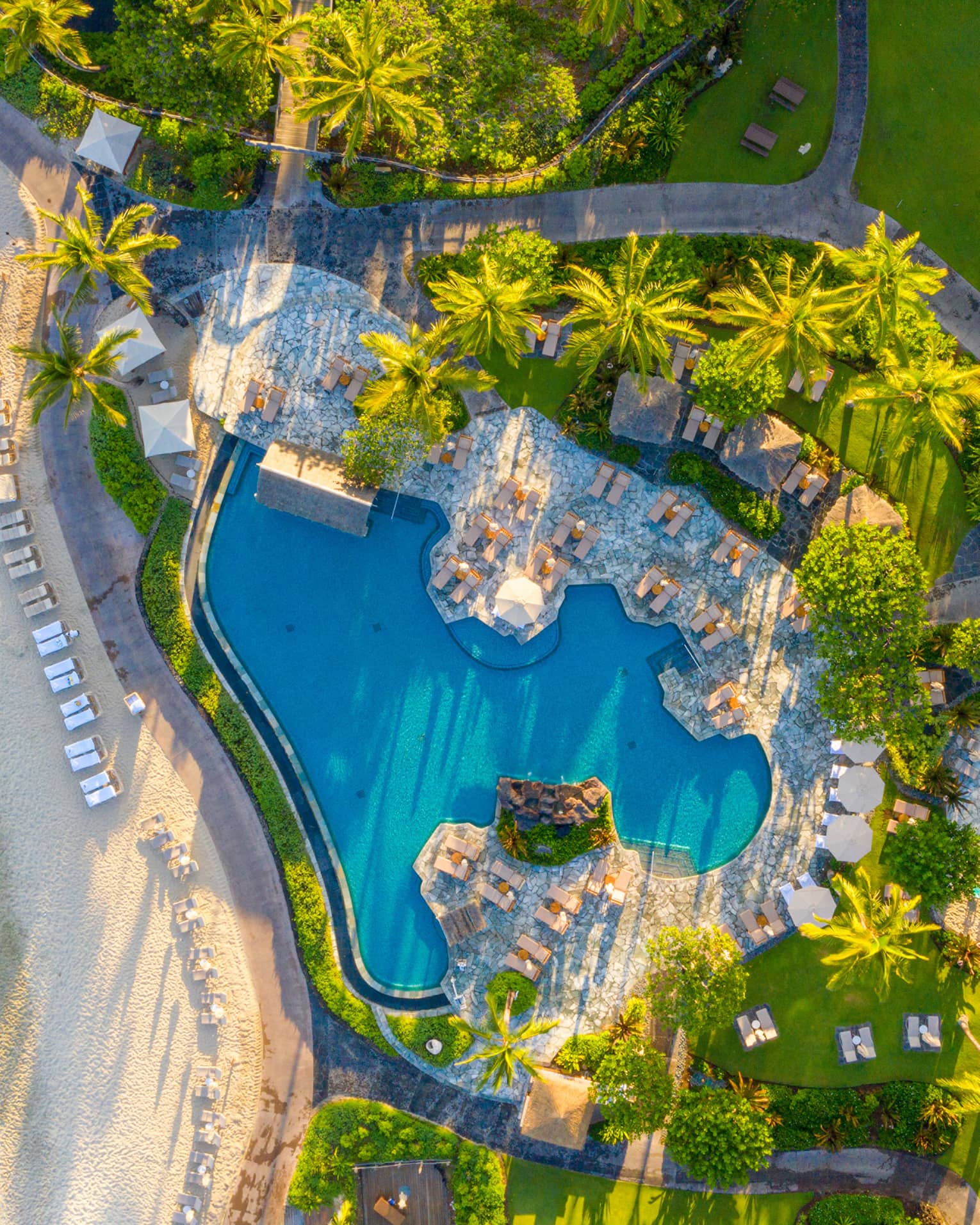 Aerial view of tropical resort pool next to a white-sand beach