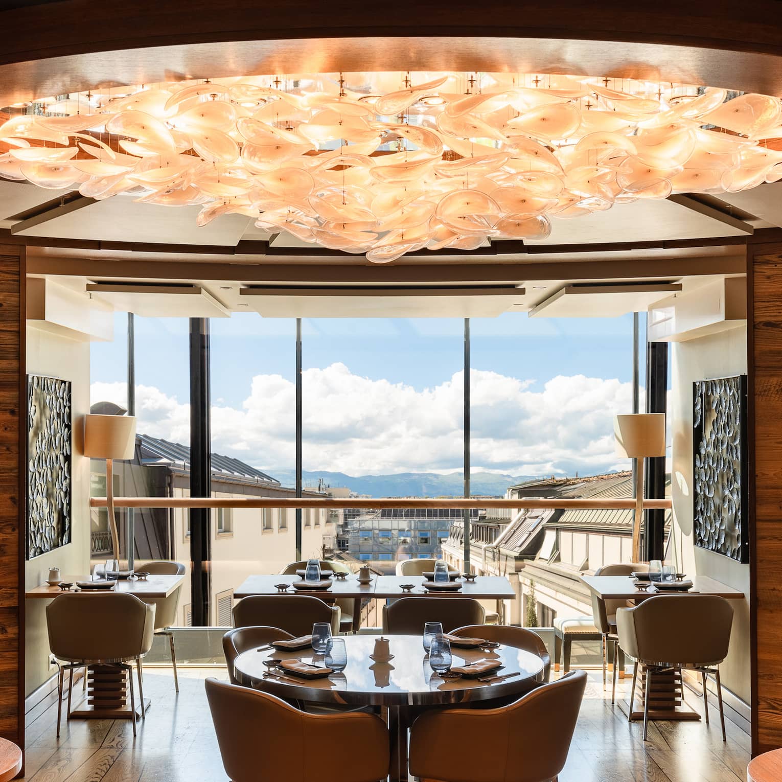 Curved, wood-panelled walls encircle a dining room with a peach-coloured chandelier and windows showing distant mountains.