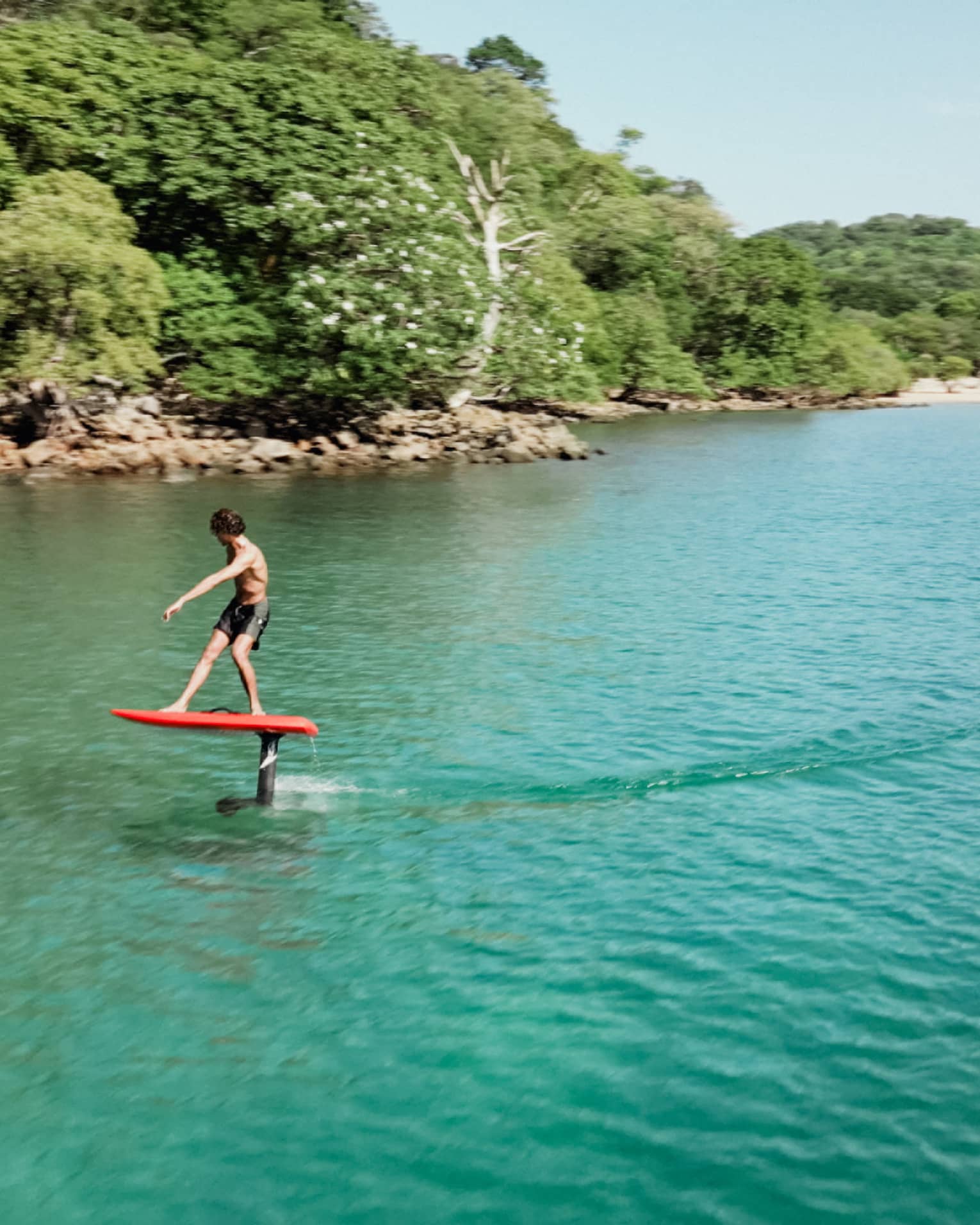 A surfer hovers over the water while riding a red e-foil surfboard