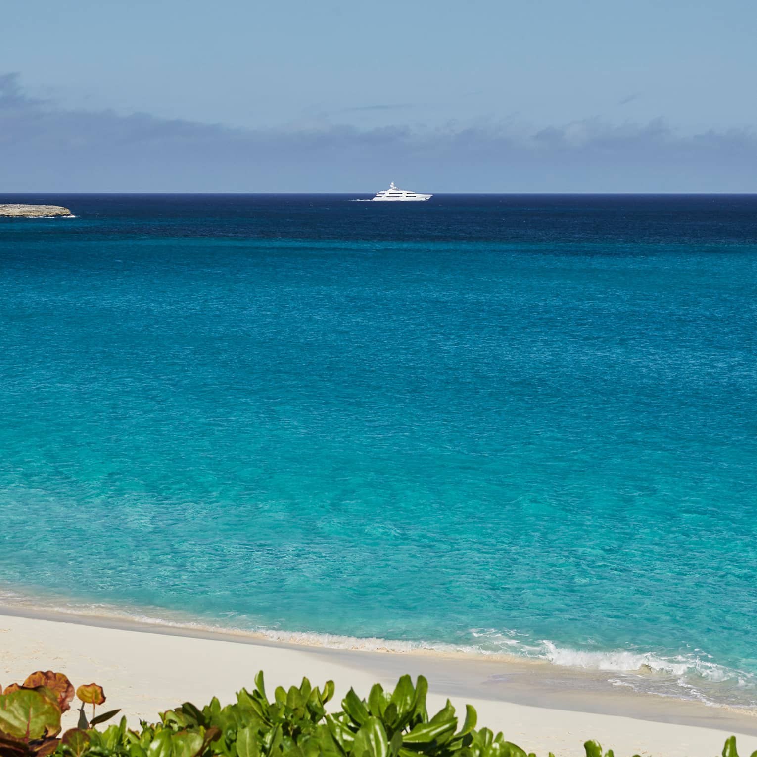 Turquoise ocean by white sand beach, yacht on horizon against blue sky