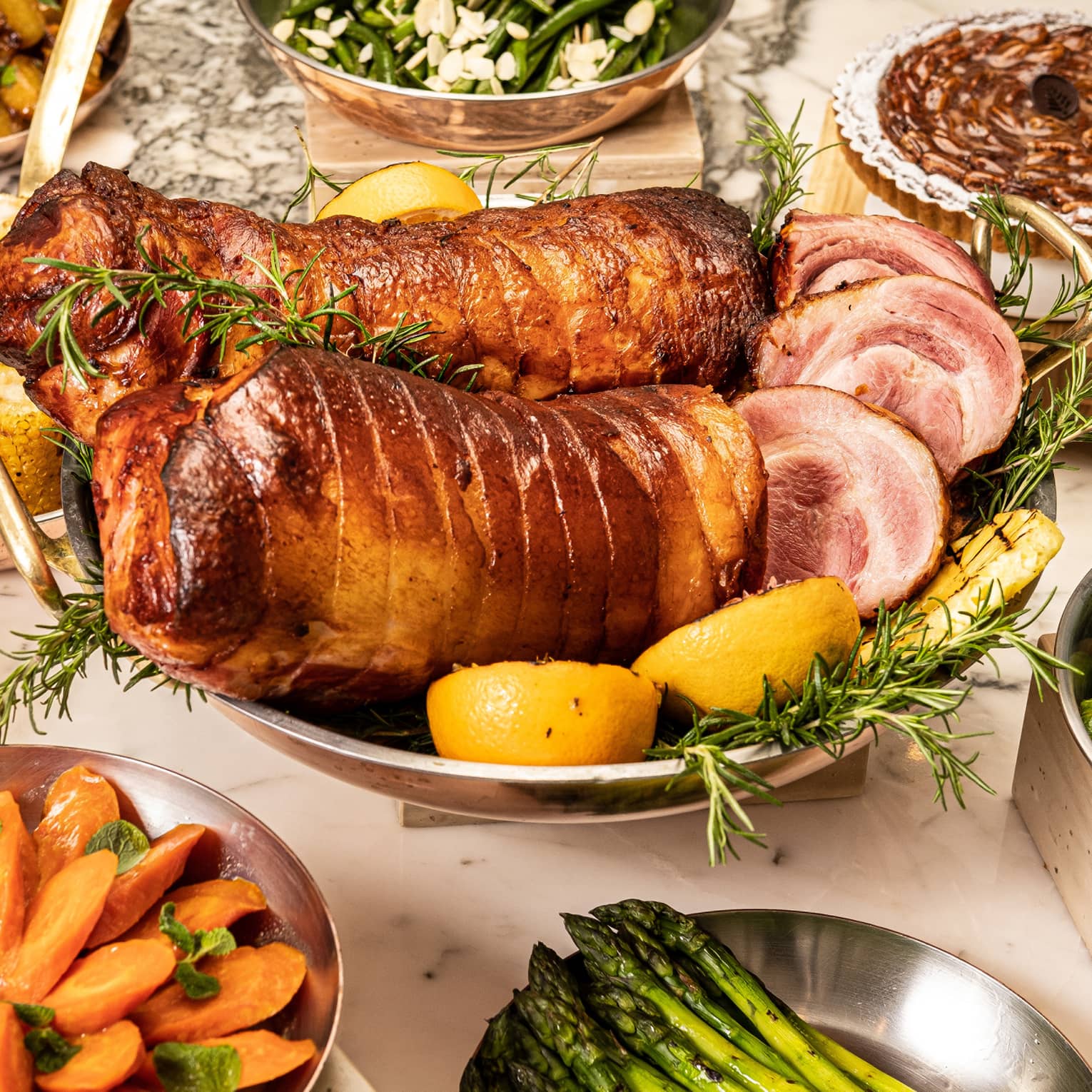 Spread of holiday dishes including porchetta, corn on the cob, roasted carrots and asparagus