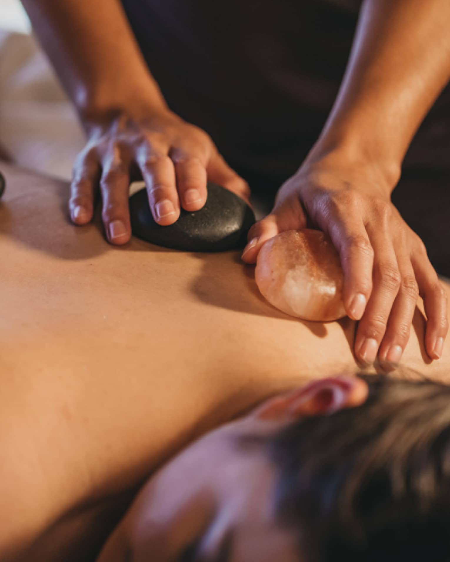 Close up of hands massaging warm stones on a woman's bare back