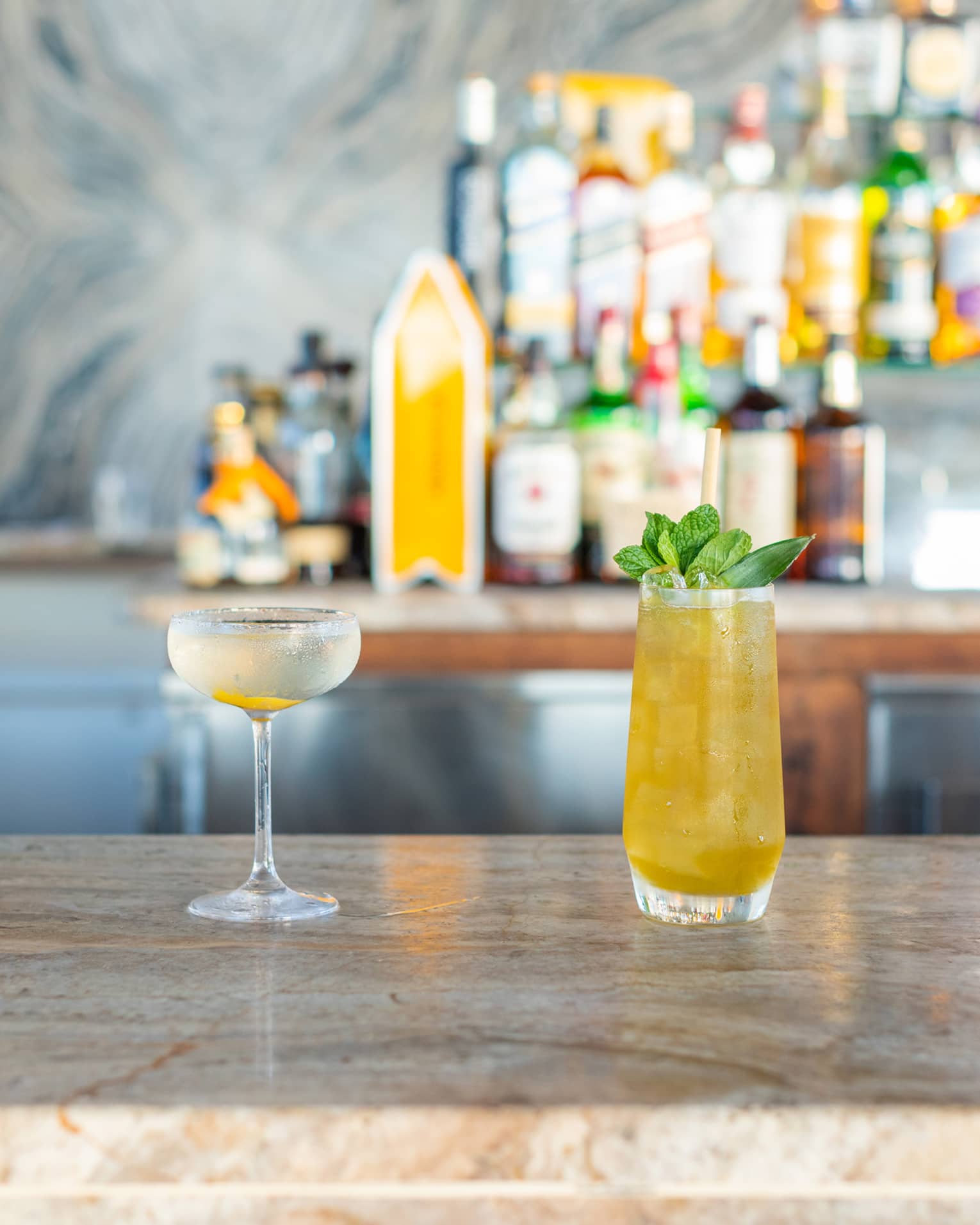 Four cocktails on a bar counter with bottles behind them.