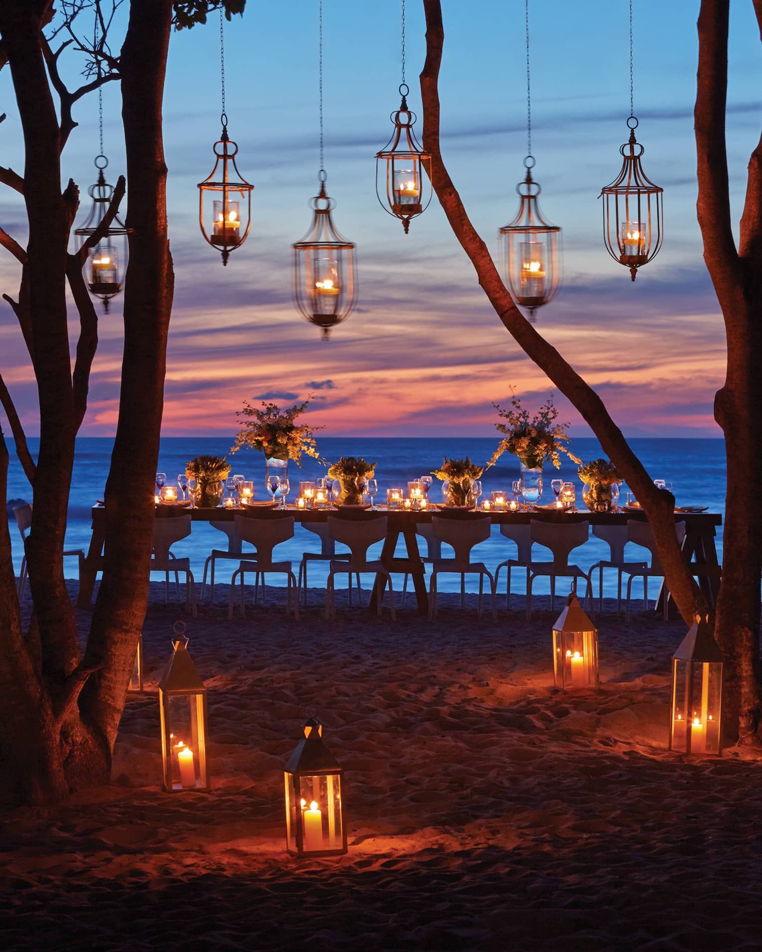 Lanterns hang from trees near dining table on Manzanillas Beach at sunset