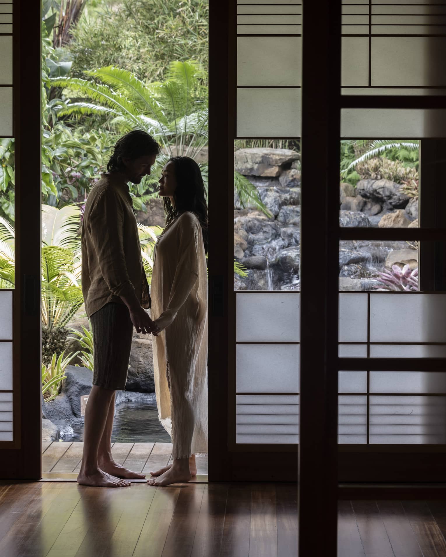 Man and woman stand holding hands in doorway of private spa hale at Sensei Lanai, A Four Seasons Resort