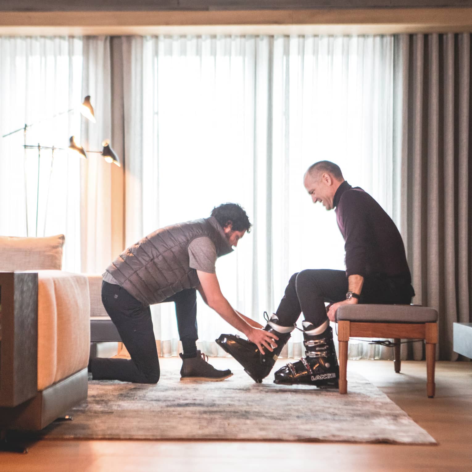 One man helping another to put on ski shoes.