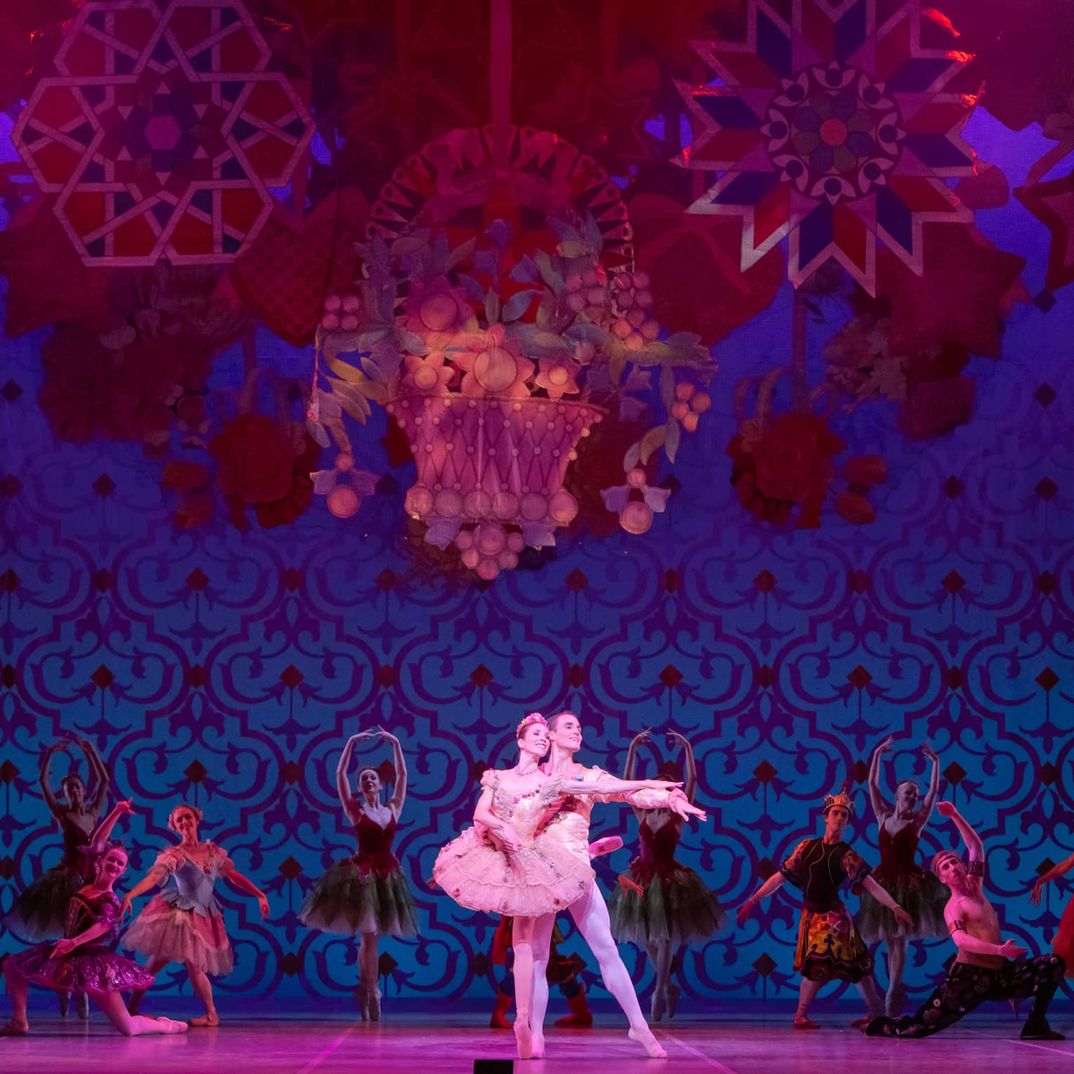 Two dancers performing ballet with back up dancers behind them in a red and blue scene.