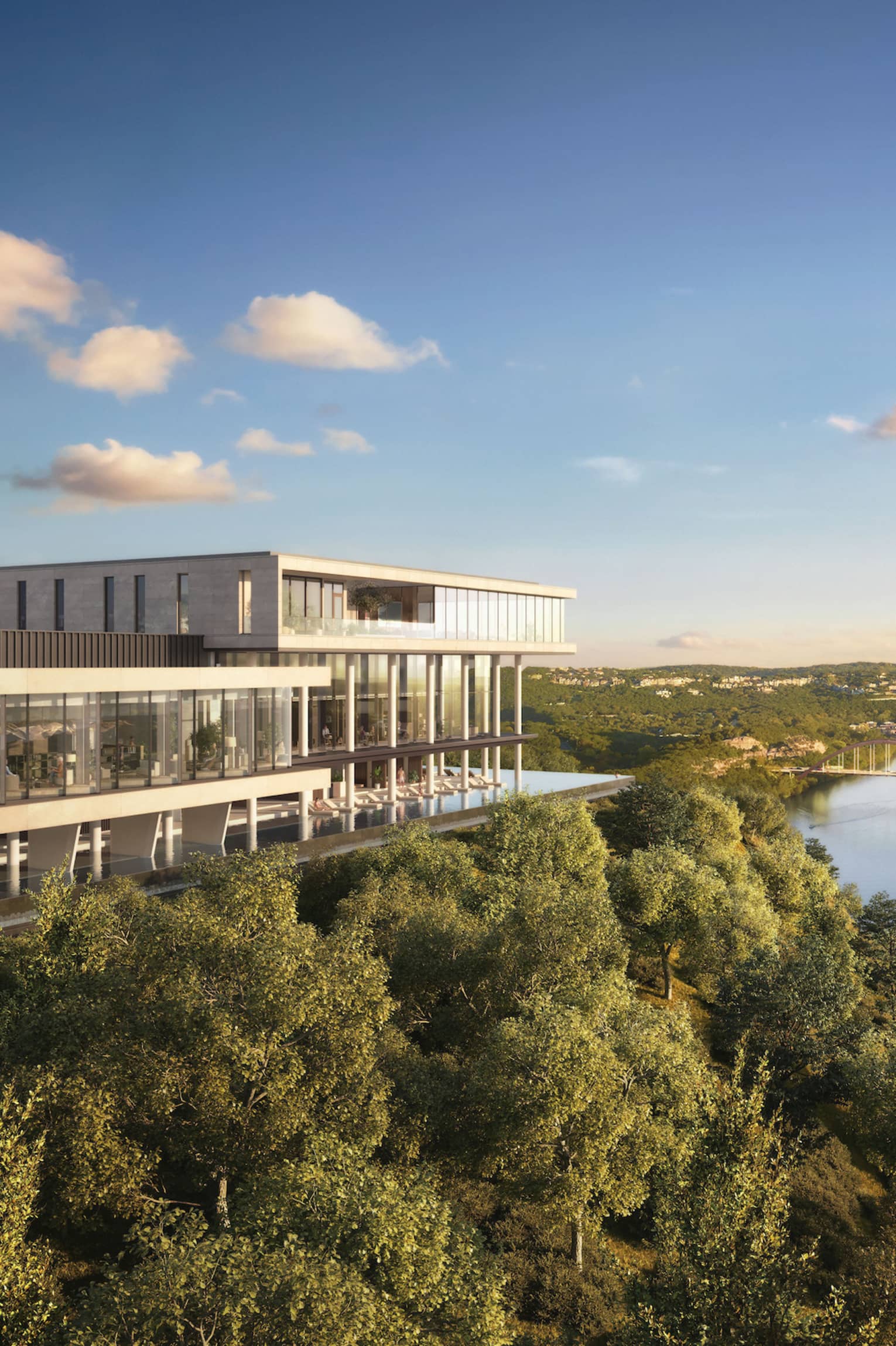 Modern building overlooks a river with a city skyline in the distance, amid lush greenery and a serene sky.