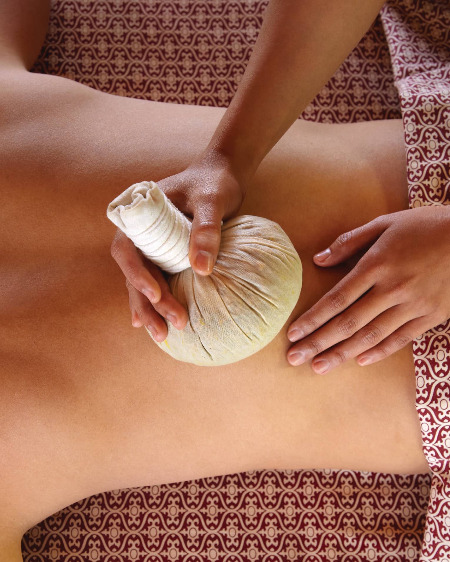 Masseuse rubs herbal sac on woman's bare back in spa