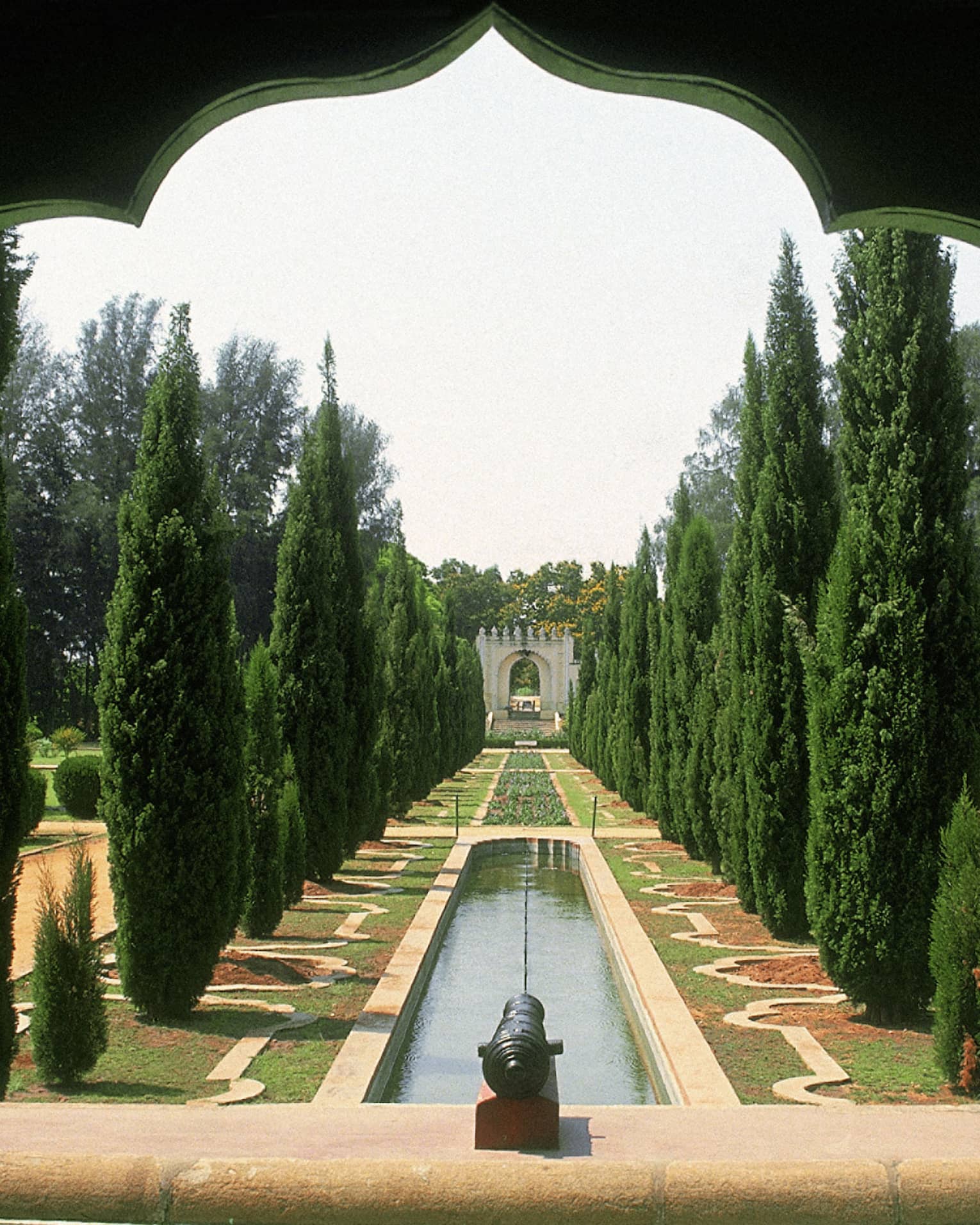 Thin trees line a strip of water and flowers in Tipu Sultan's Gardens