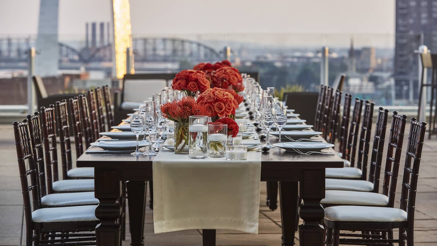 Long private dining table with red flowers on rooftop with Gateway Arch view