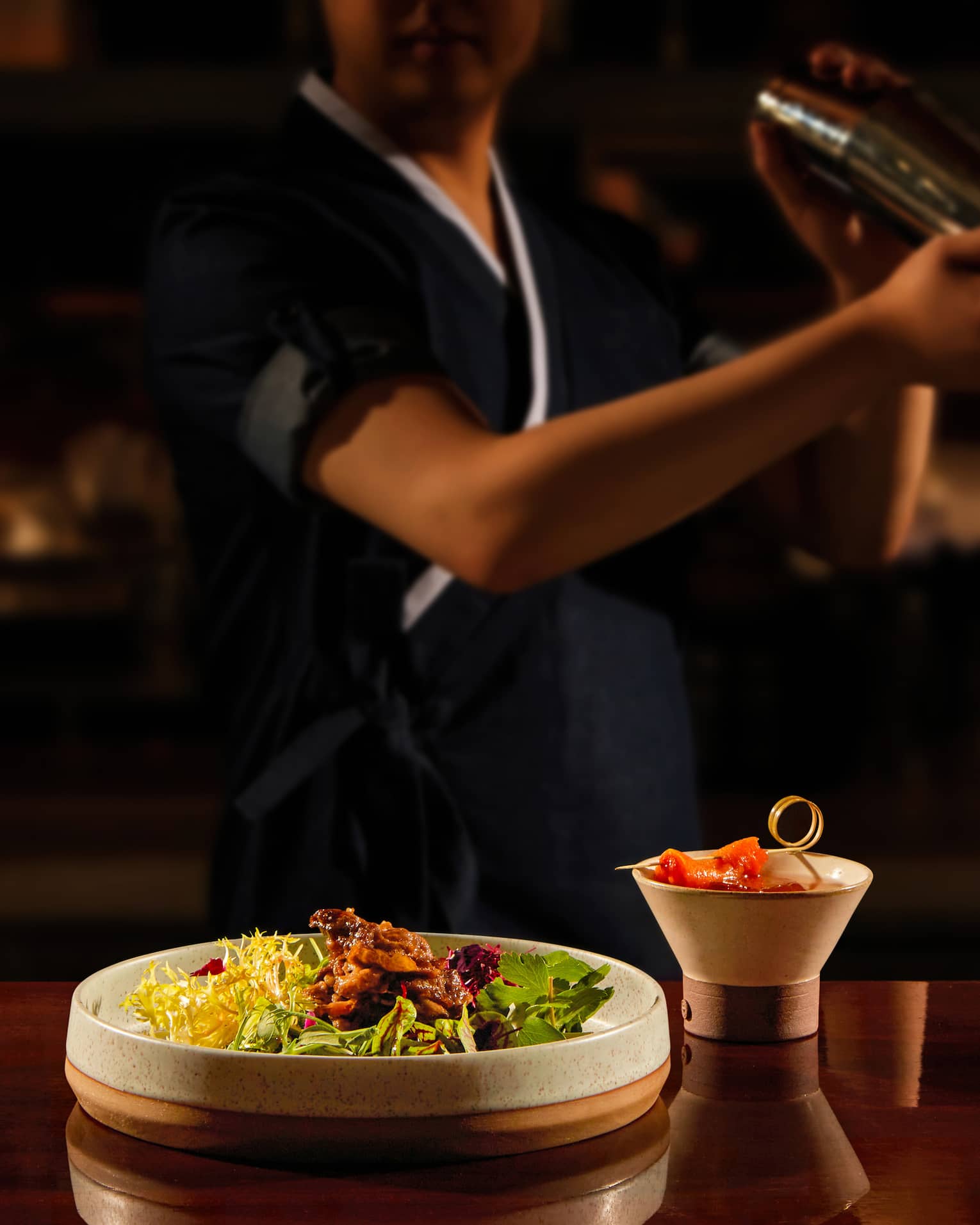Bartender shaking a cocktail, bar bites at the forefront