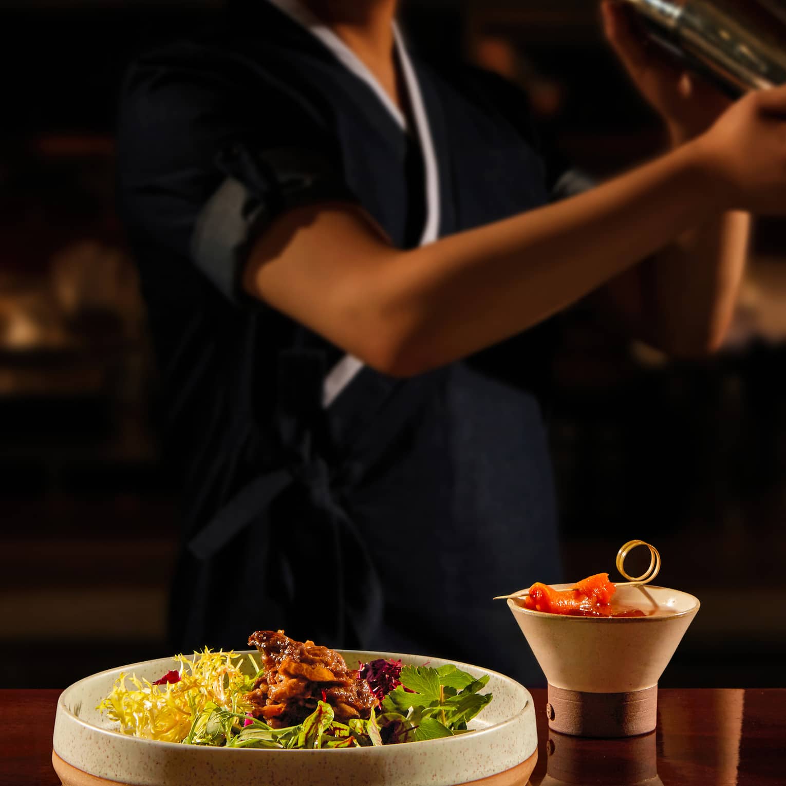 Bartender shaking a cocktail, bar bites at the forefront