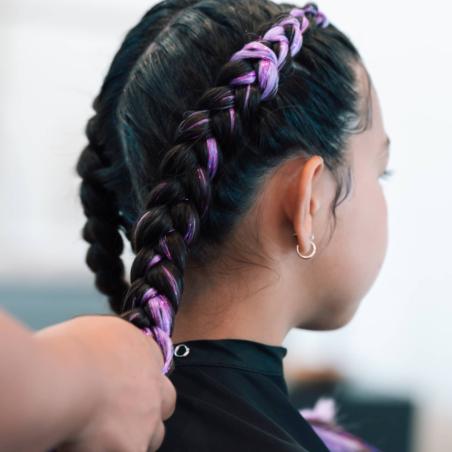 A young girl gets her hair braided with light purple interwoven color