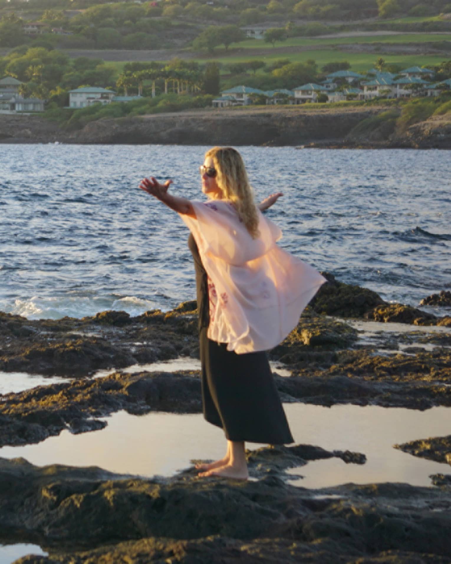 A woman meditates at edge of ocean on lava rock