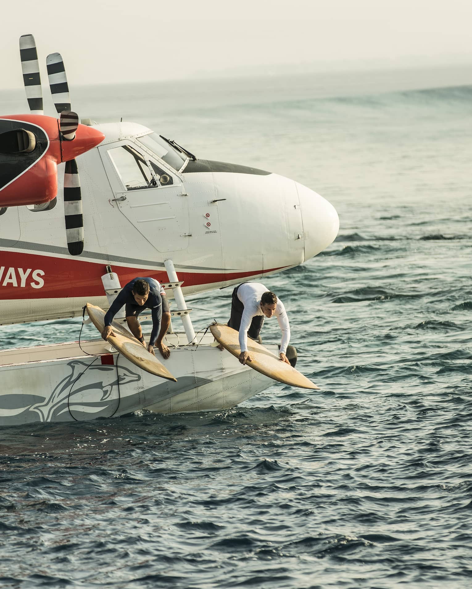 Two people with surfboards jump from float plane onto waves