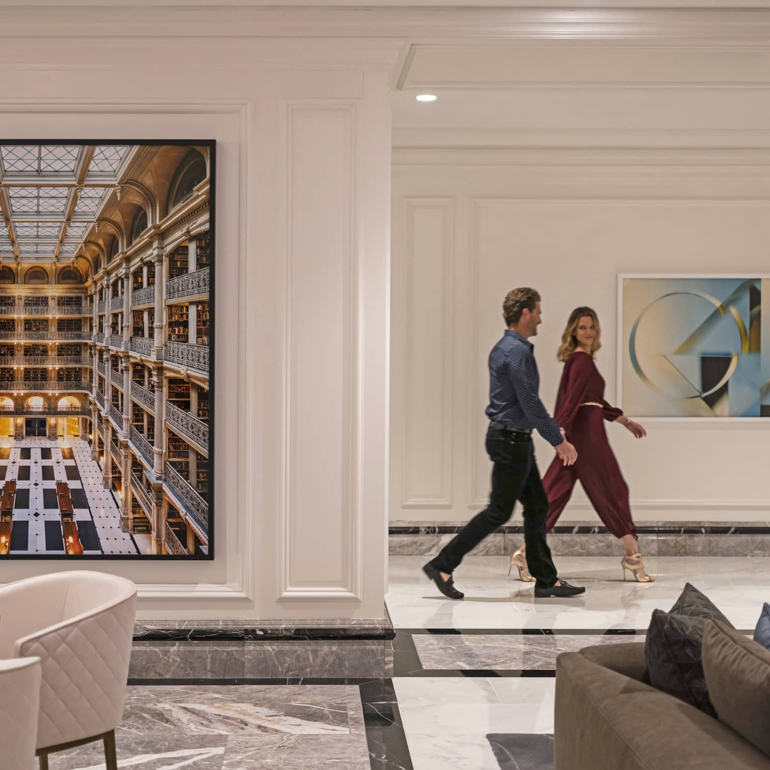 A couple walking through the hotel lobby, there is art on the wall behind them.