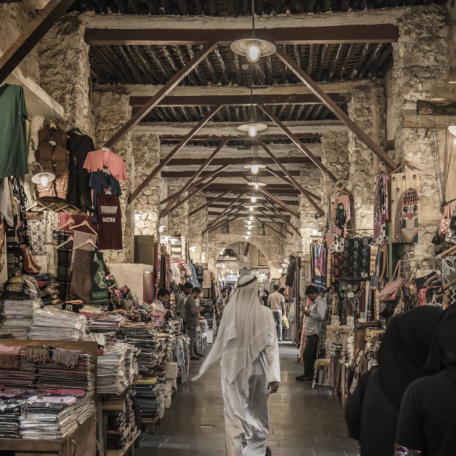 People walk past tables with textiles, clothes in indoor market