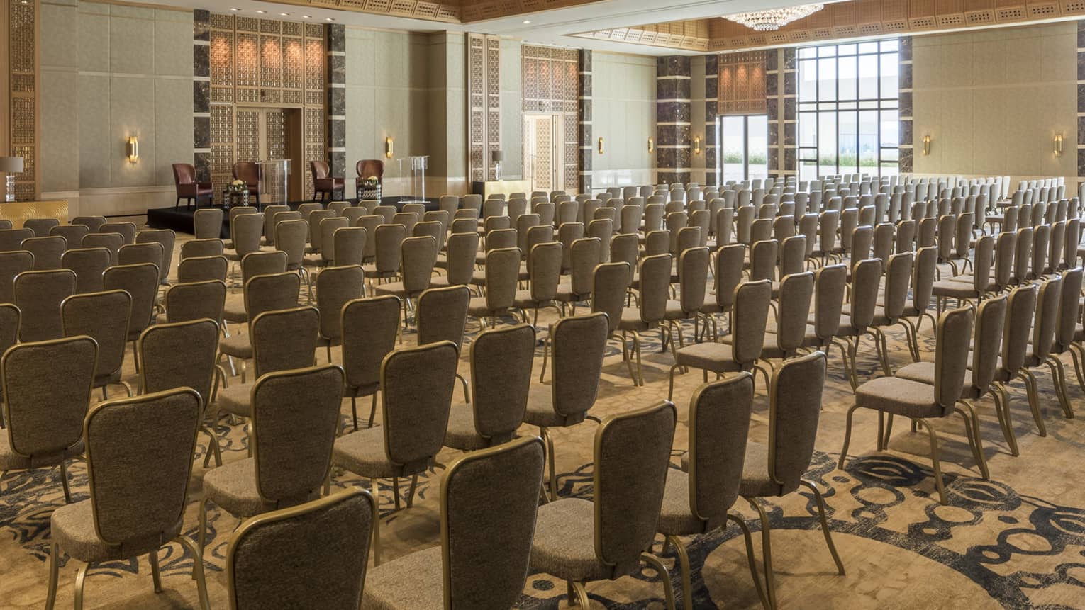 Chairs arranged in rows facing raised stage in Jasmin Ballroom accented with gold and large chandeliers 