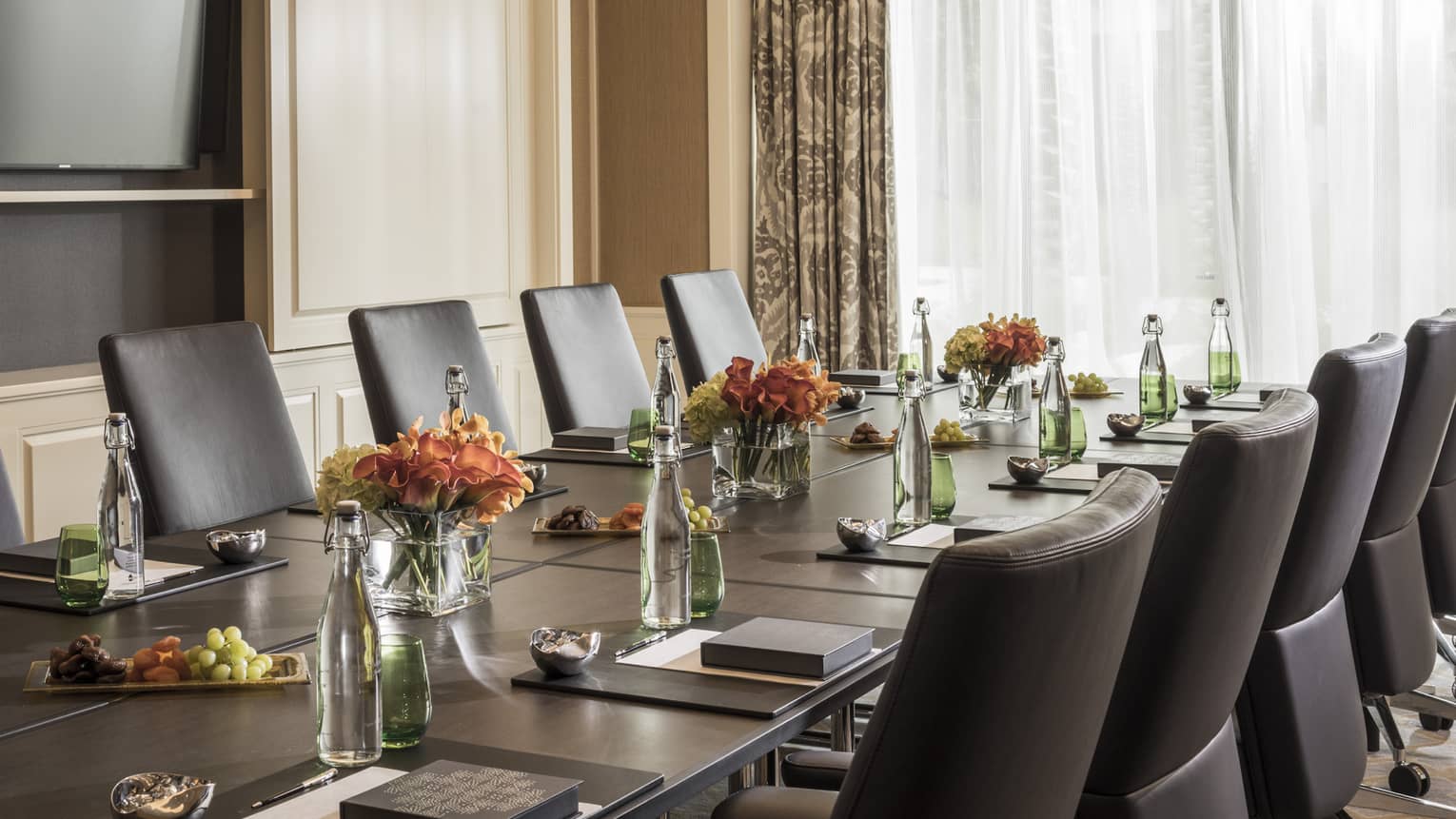 Long boardroom table set with glass bottles of water, flowers in bright meeting room