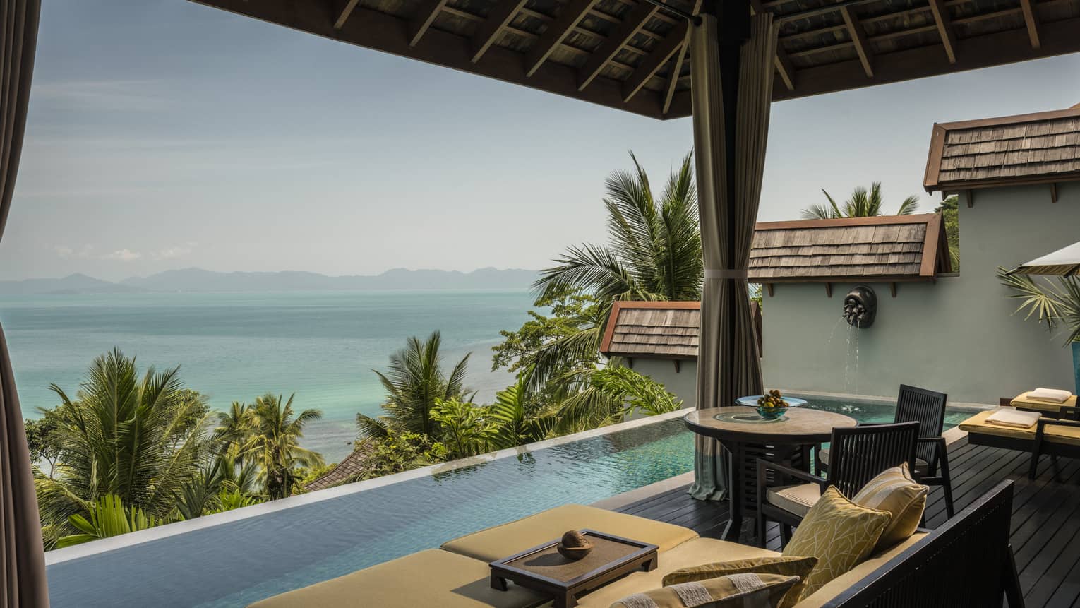 Patio chairs, cushions by infinity swimming pool on villa deck