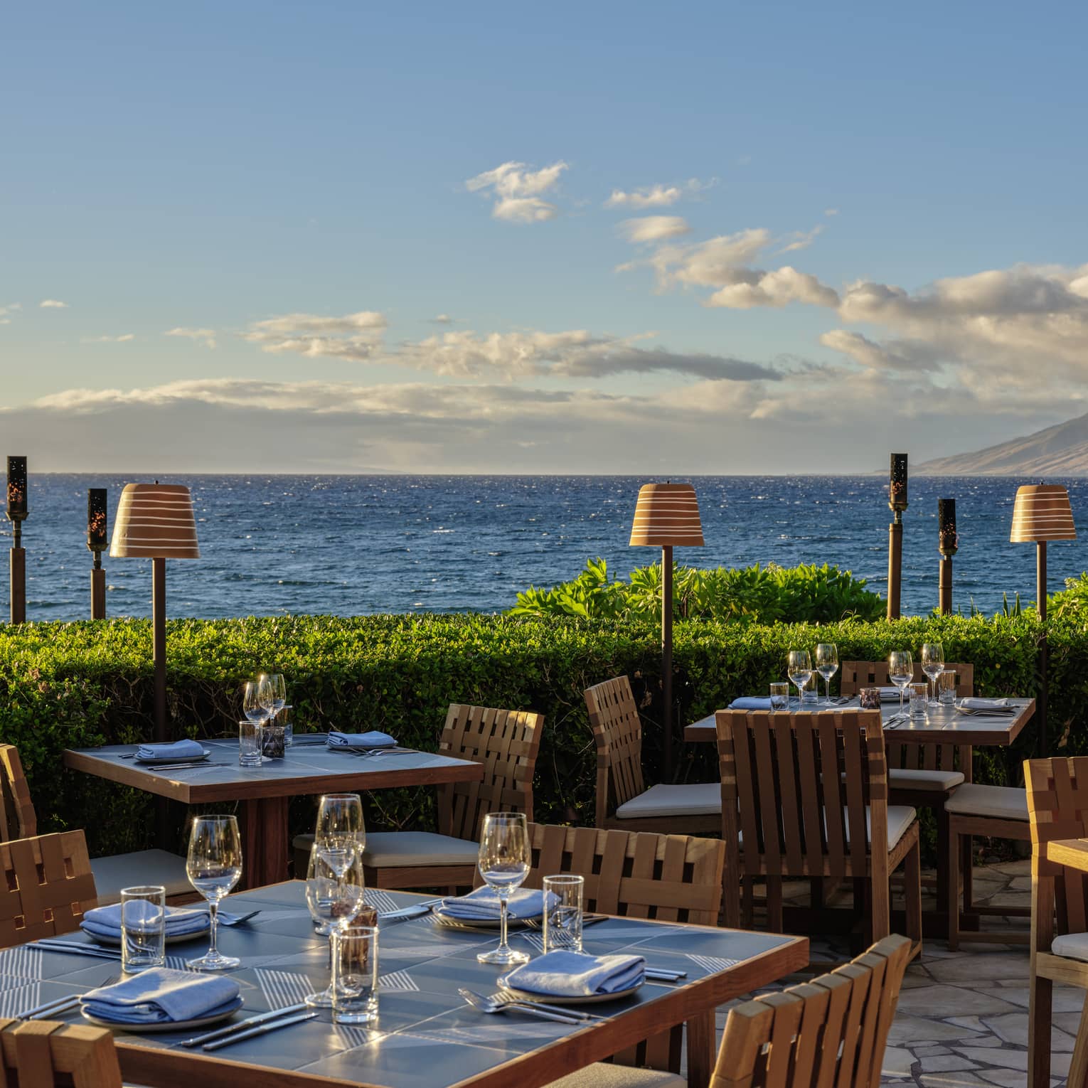 Oceanfront outdoor dining area with wooden tables and chairs set for service