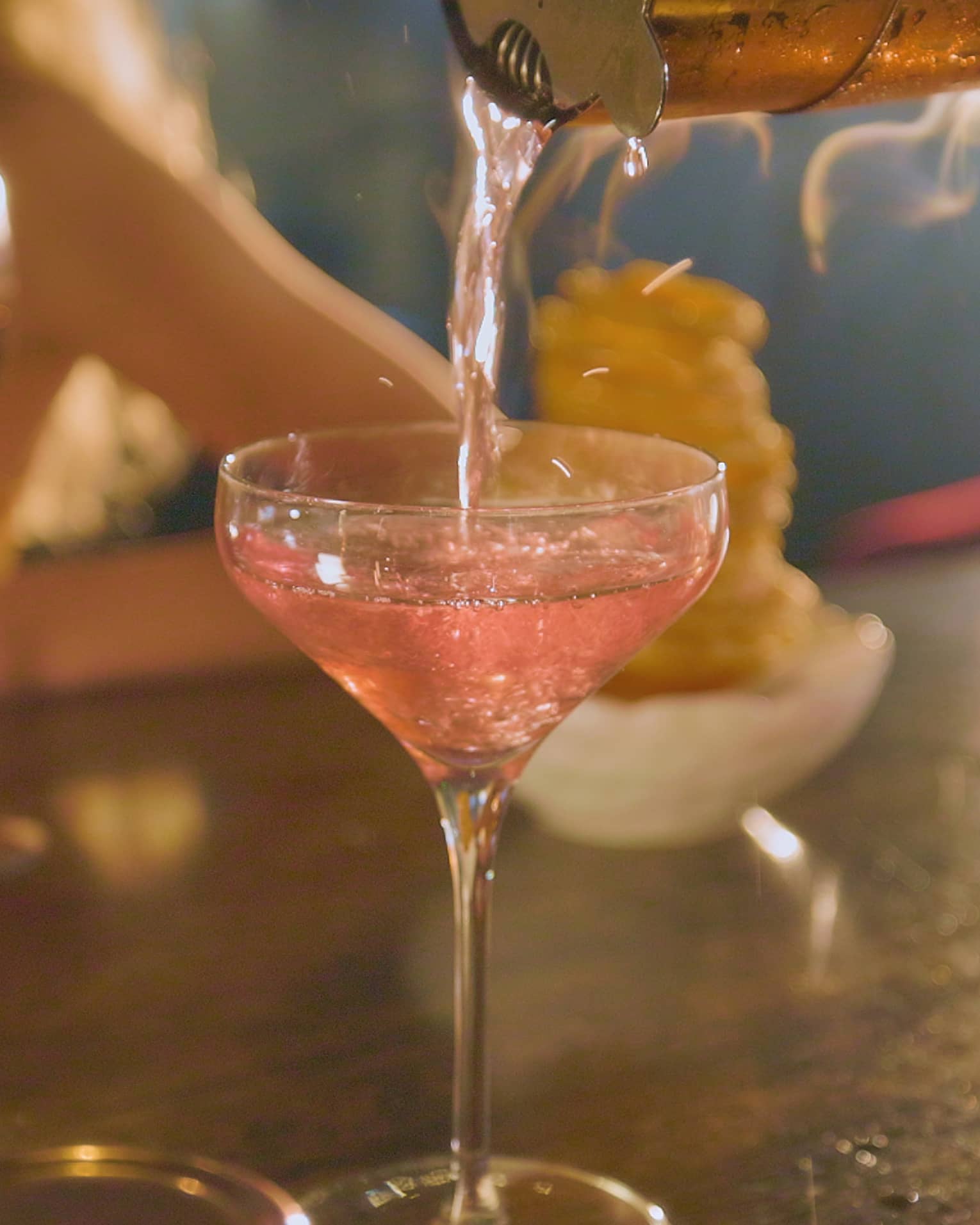 Pink beverage being poured into a cocktail glass
