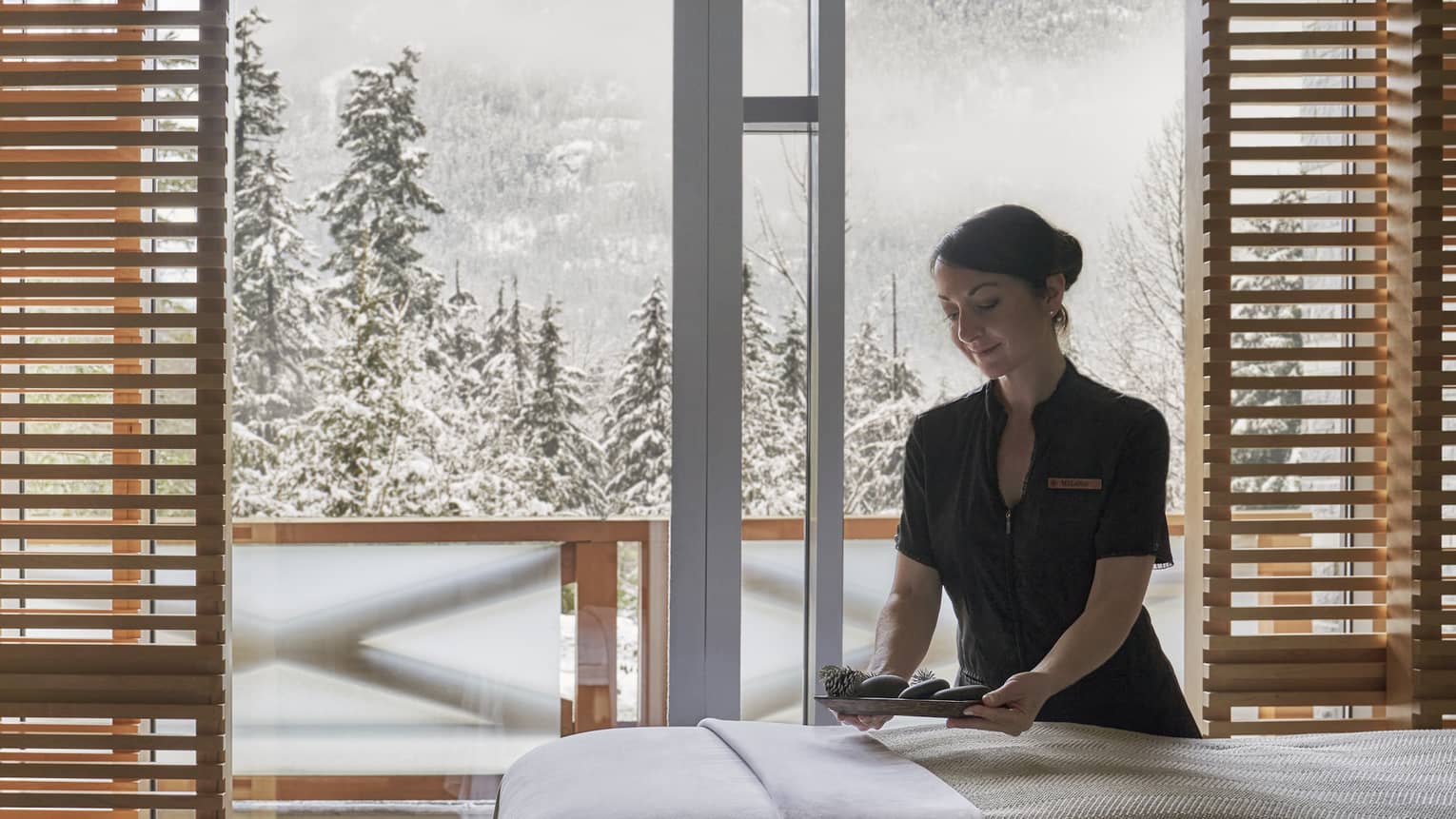 Spa staff smooths sheet on massage table in front of window with winter view