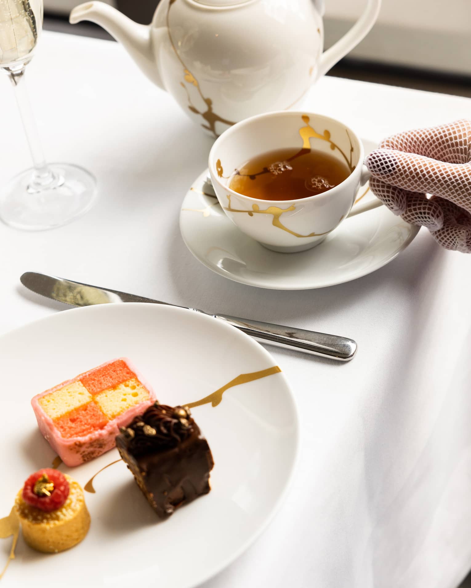 A woman picking up a cup a tea with a plate of small treats next to it.