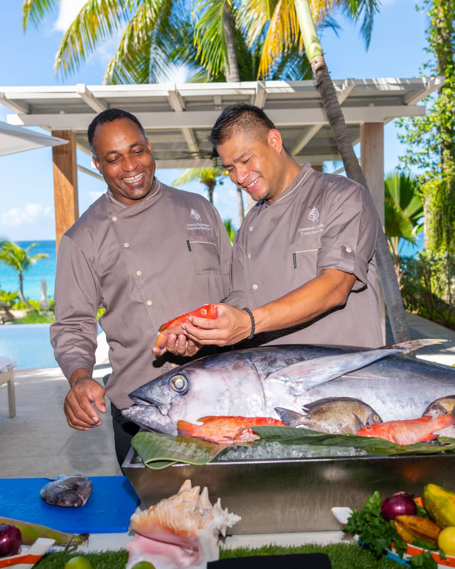 Two people standing in front of a food display with a large fish while holding a smaller fish.