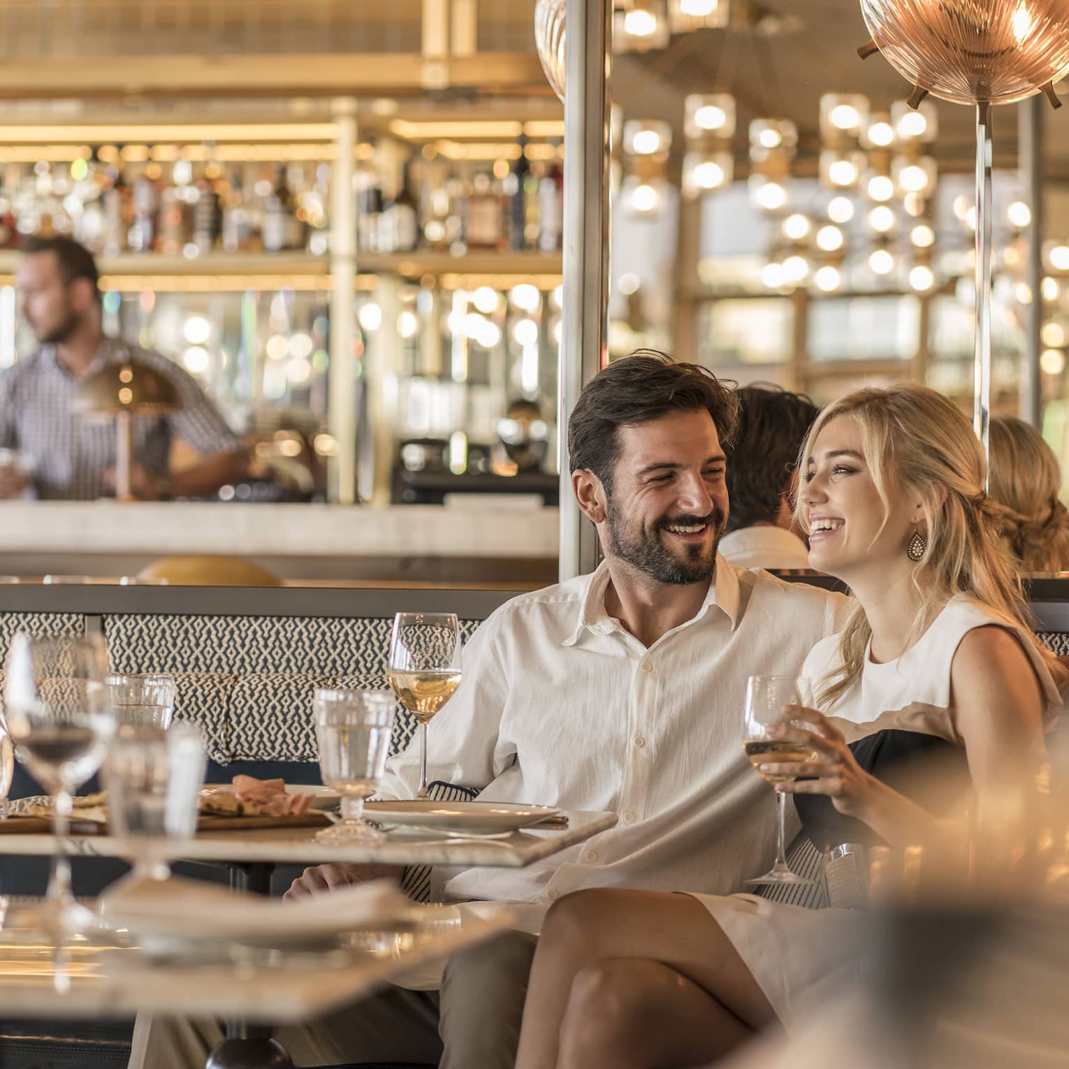 Smiling couple drink wine in a booth of a luxurious restaurant decorated in an elevated neutral and bronze colour palette.