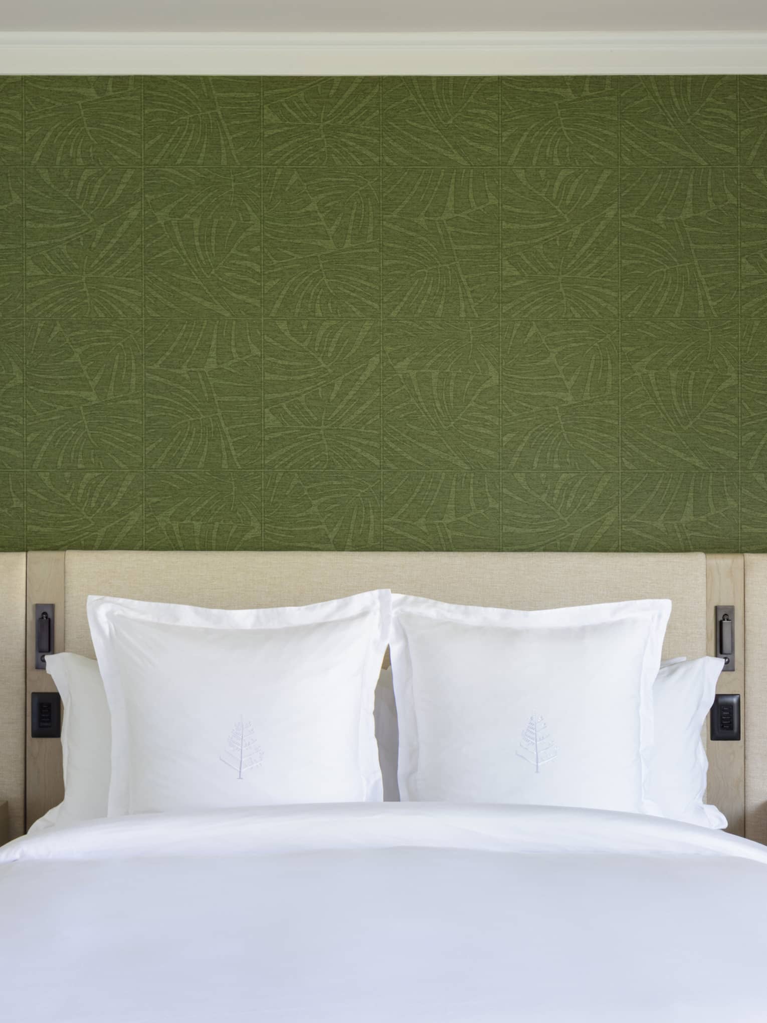 King bed with white sheets and Four Seasons logo on the pillows, set against green wallpaper