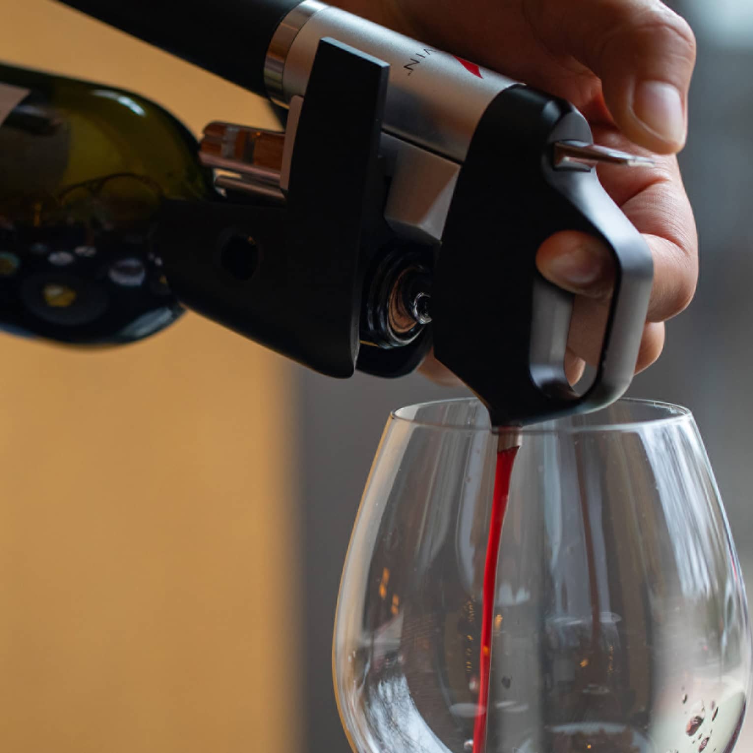 Their hands holding the bottle steady, a person pours scarlet red wine through an aerator device into a glass.